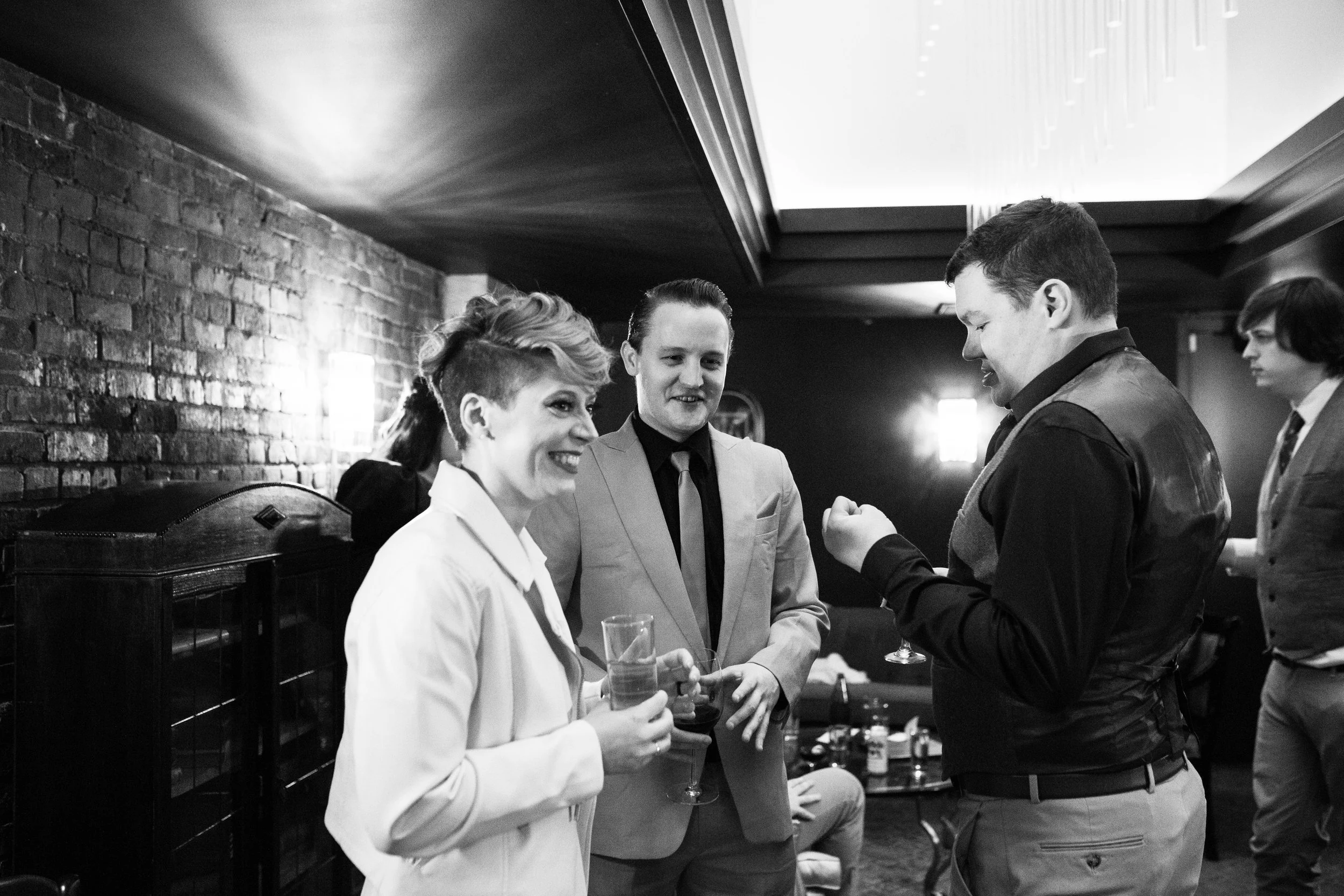 Group of four people talking and smiling at an indoor social event, holding drinks. Pioneer Square, Seattle, WA wedding photography.