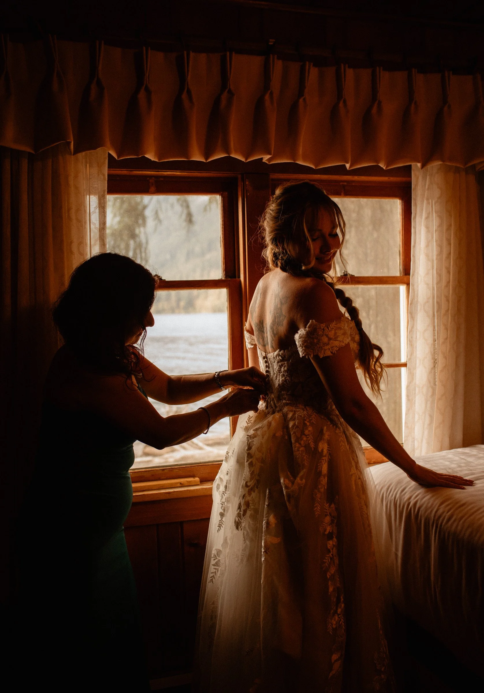 Mother of the bride helping her daughter into her dress inside the Lake Crescent Lodge bridal suite at Lake Crescent in Port Angeles, Washington.