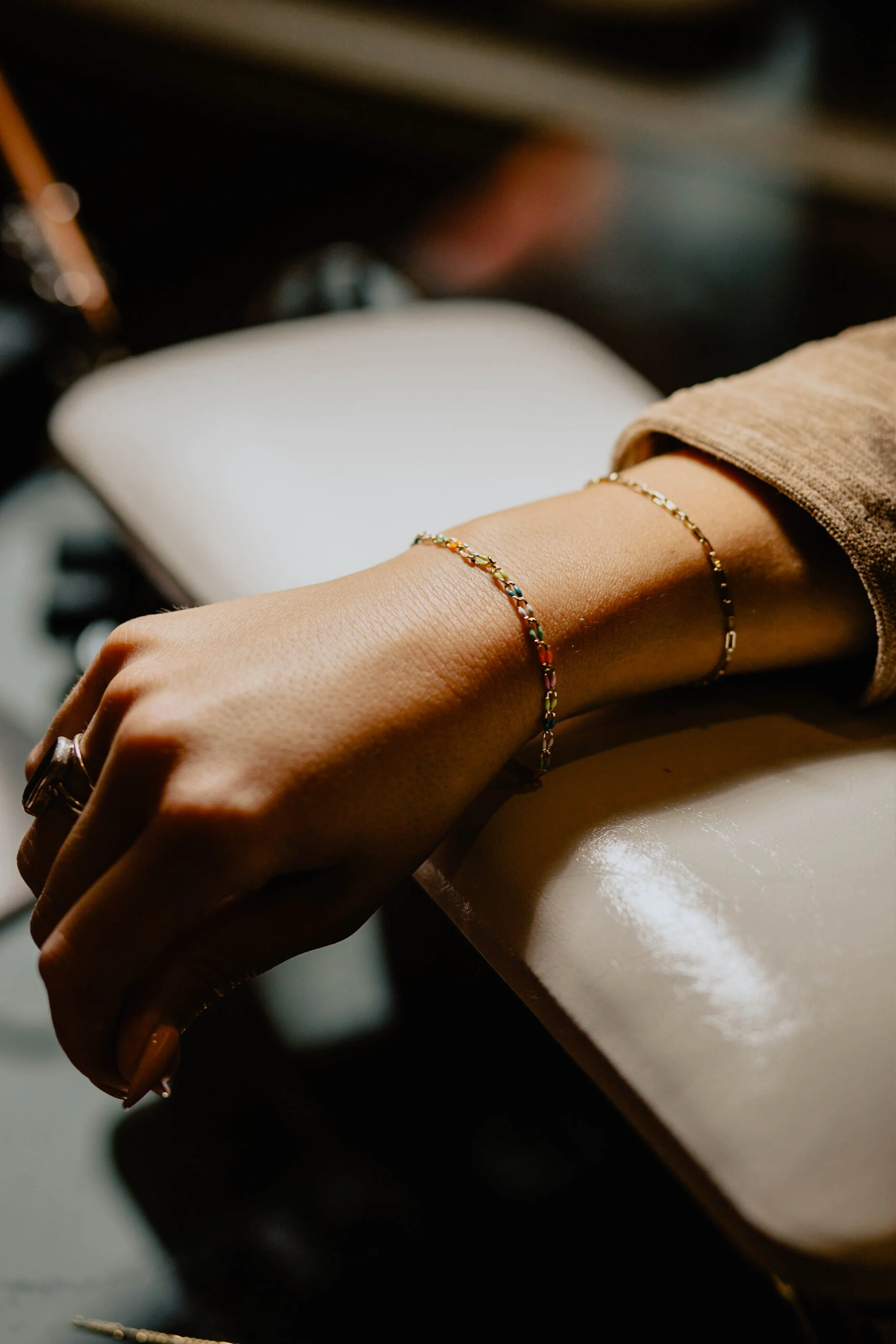 Close-up of a woman's hand resting on a white surface, wearing delicate gold and multicolored gemstone bracelets and rings. Seattle professional head shot photography