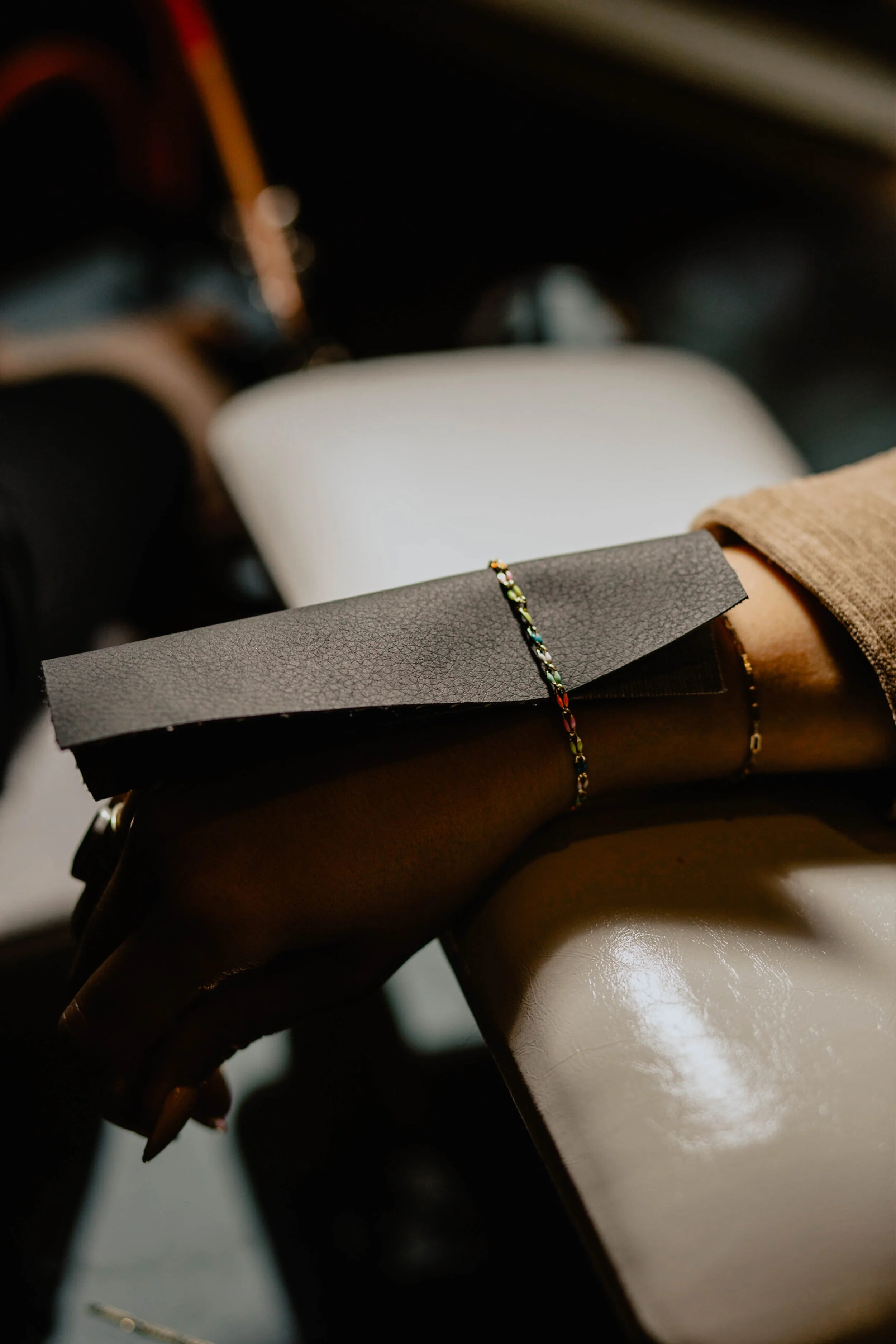 A hand with long nails holds a black paper with a colorful bracelet on the wrist, resting on a shiny beige table. Seattle professional head shot photography