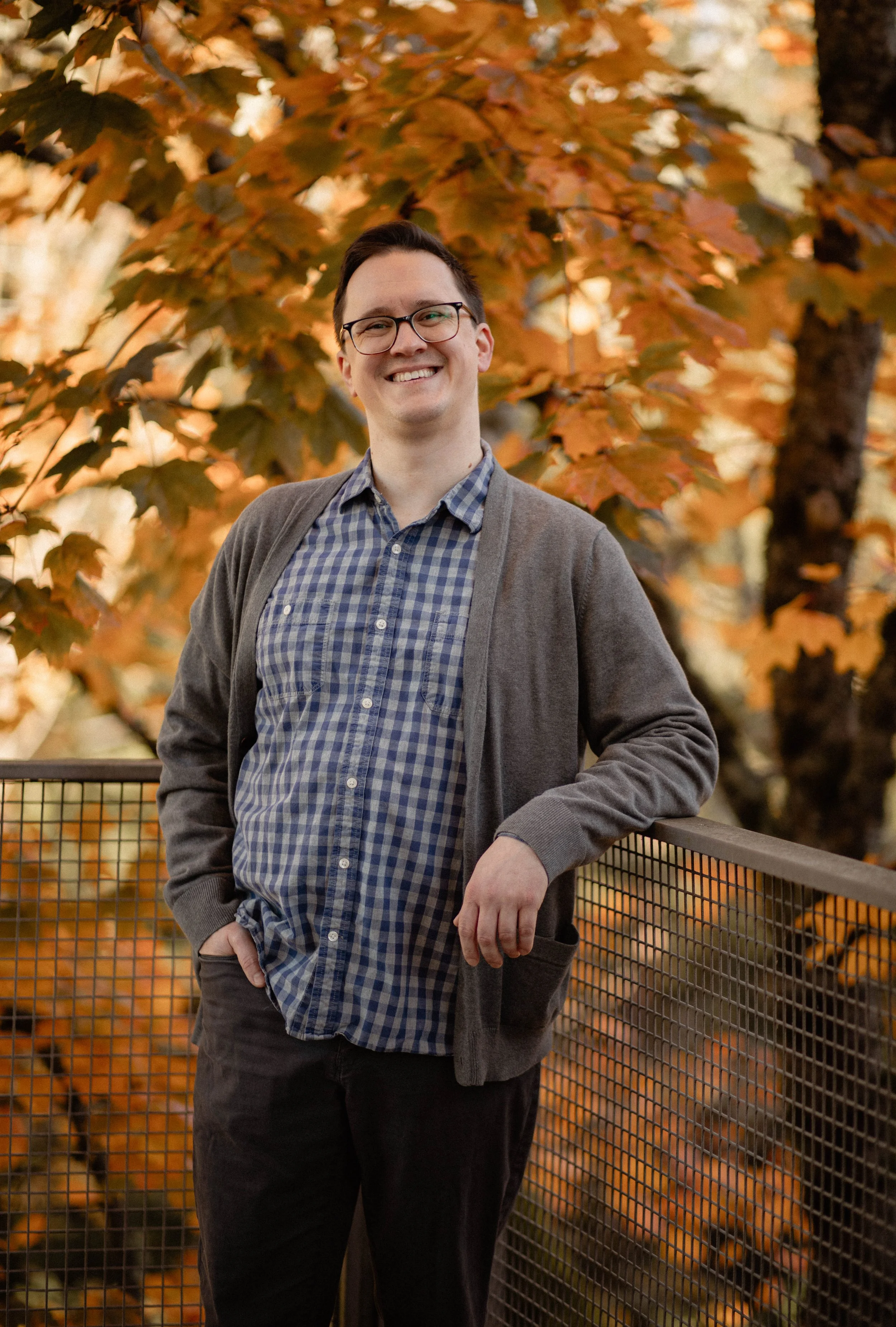 A man with glasses smiling outdoors during fall, standing next to a railing with orange-leaved trees in the background. Seattle professional head shot photography