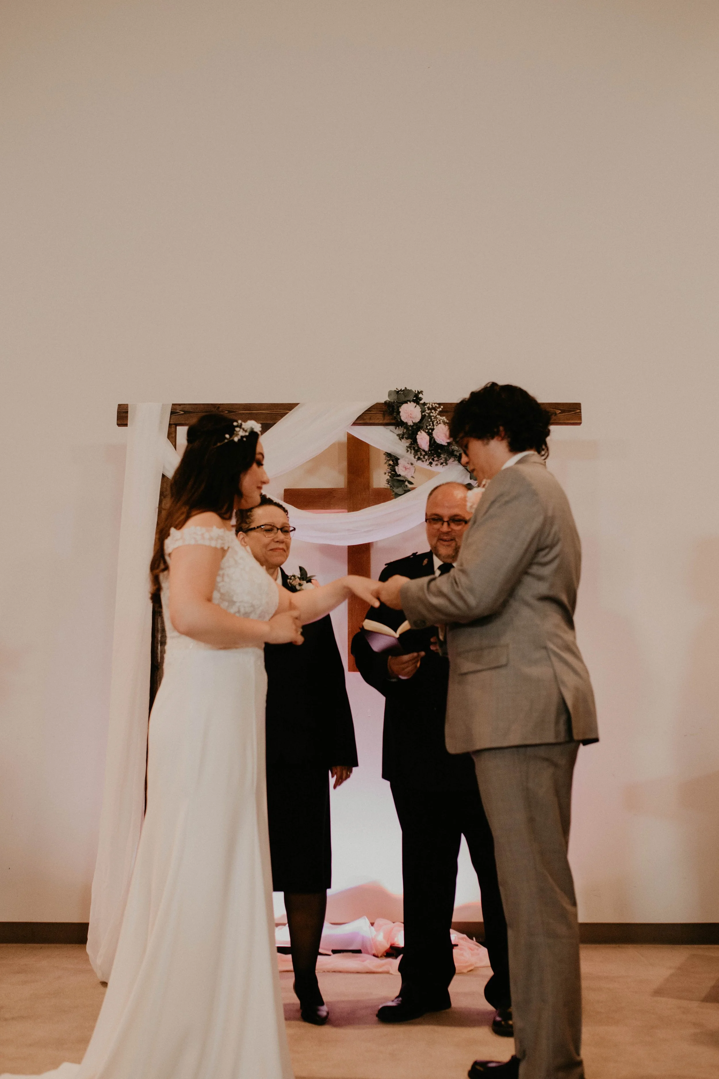 A wedding ceremony with a bride and groom exchanging rings, officiated by a person holding a book, with floral decorations in the background. Seattle, WA wedding photography.