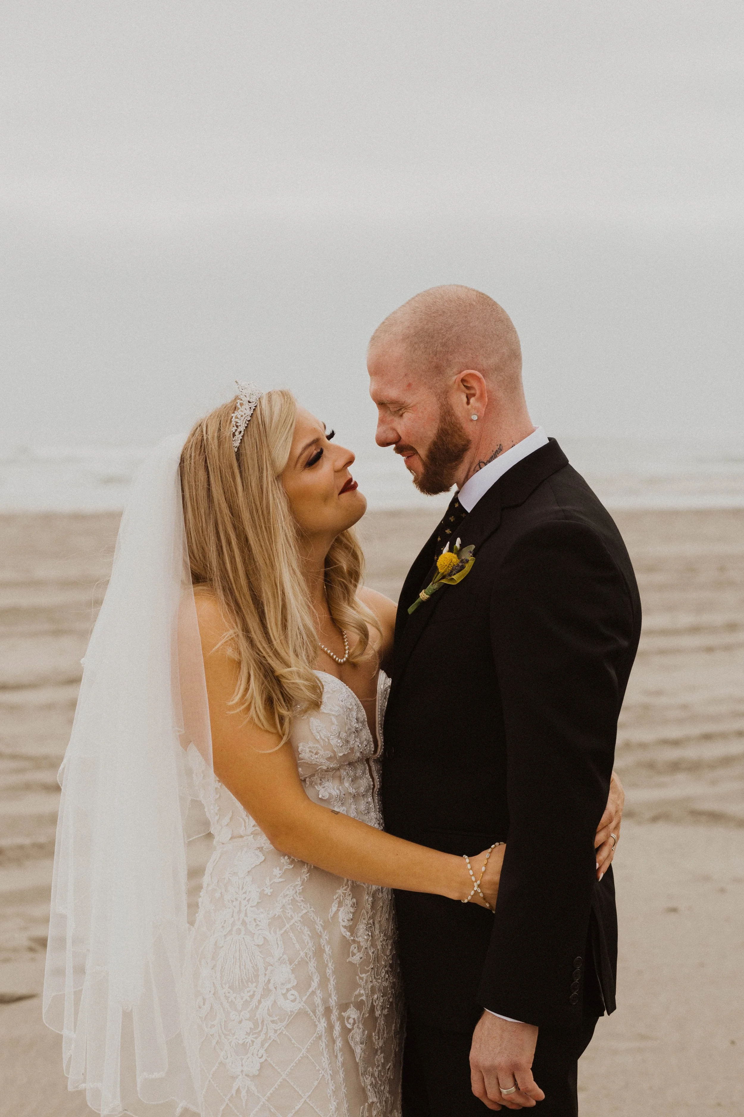 A bride and groom standing close on a beach, looking into each other's eyes, with ocean waves in the background during their wedding. Long Beach, WA wedding photography.
