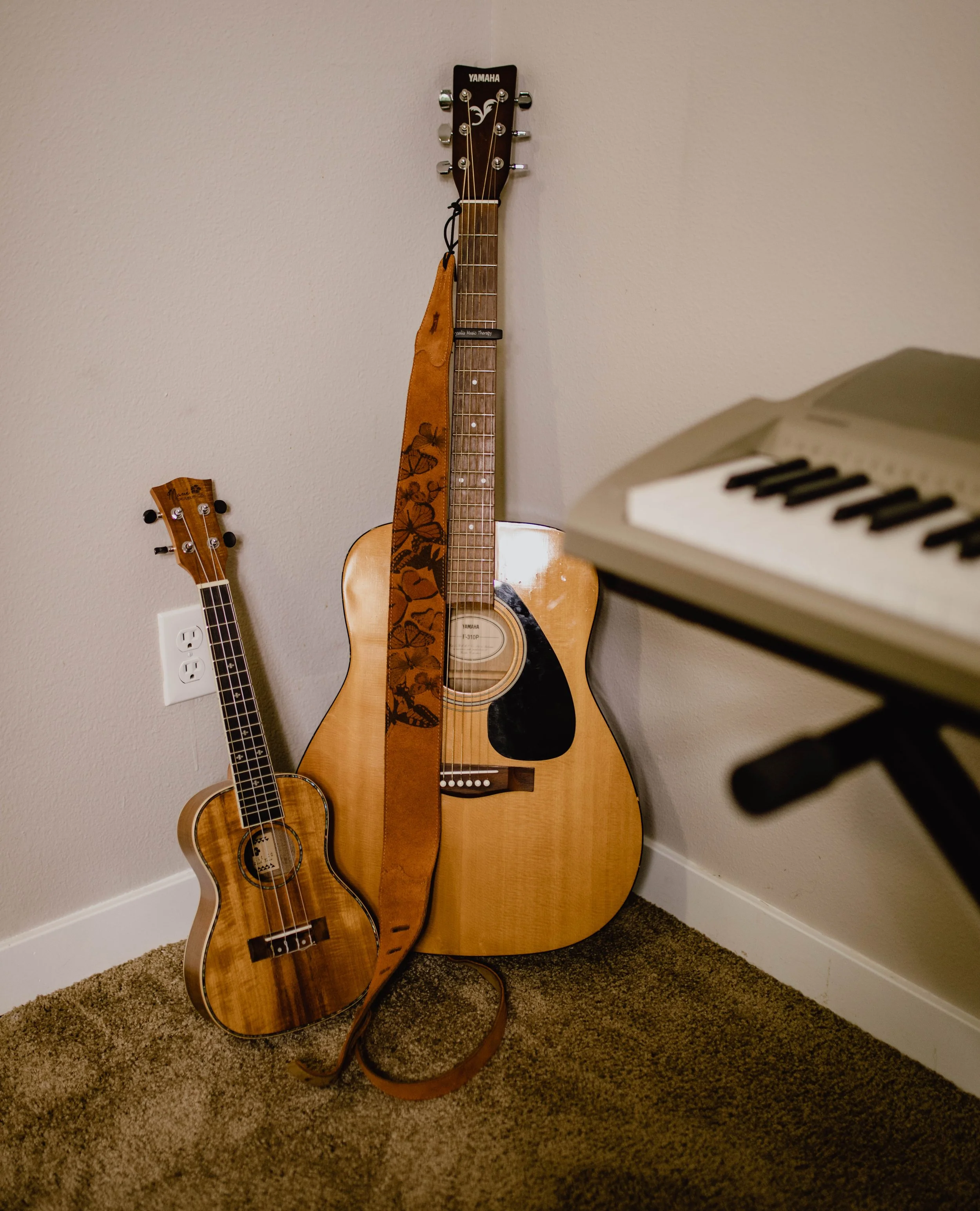 Two acoustic guitars, a small ukulele, and a keyboard in a room with beige walls and carpet. Seattle professional head shot photography