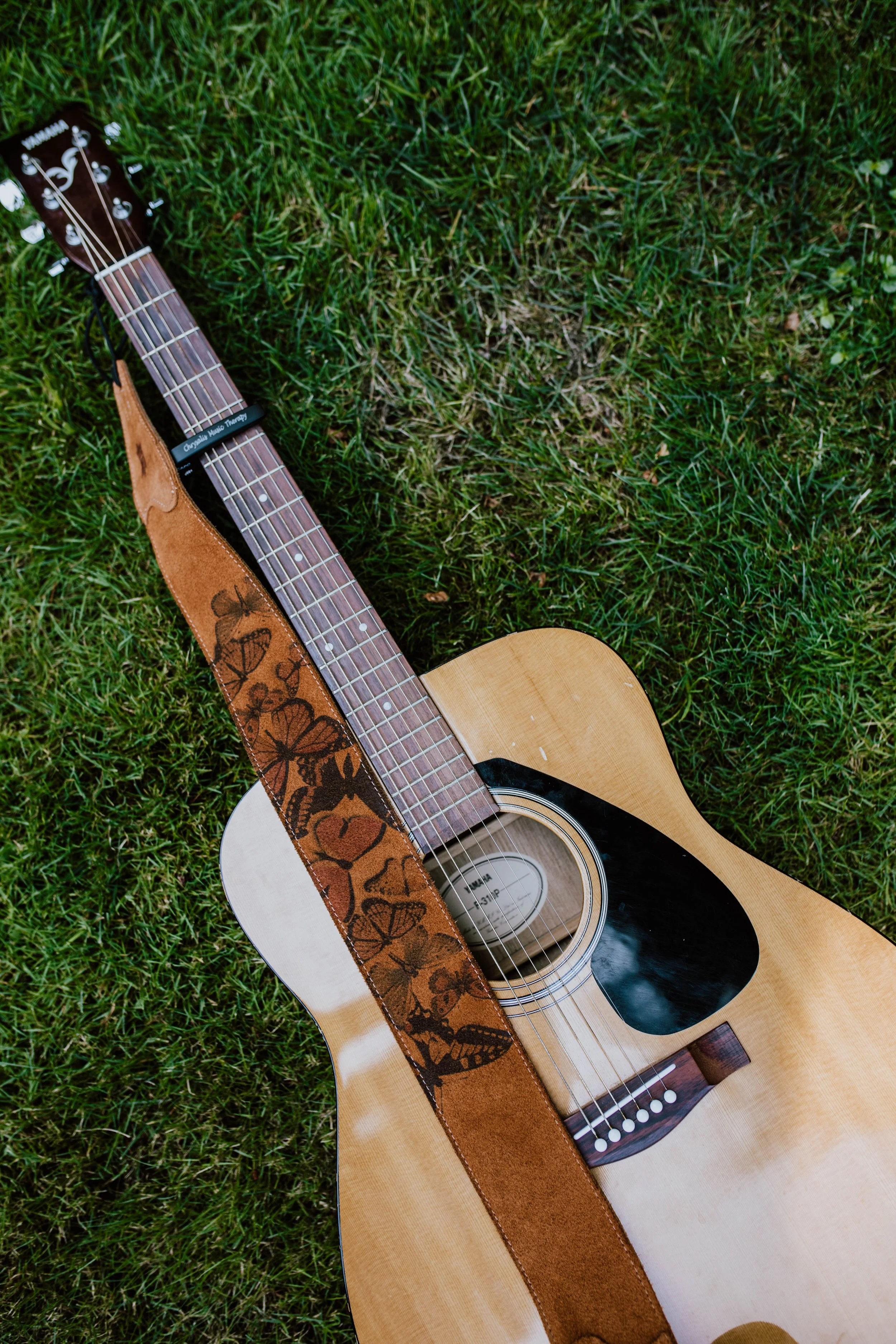 Acoustic guitar lying on grass with a floral strap. Seattle professional head shot photography