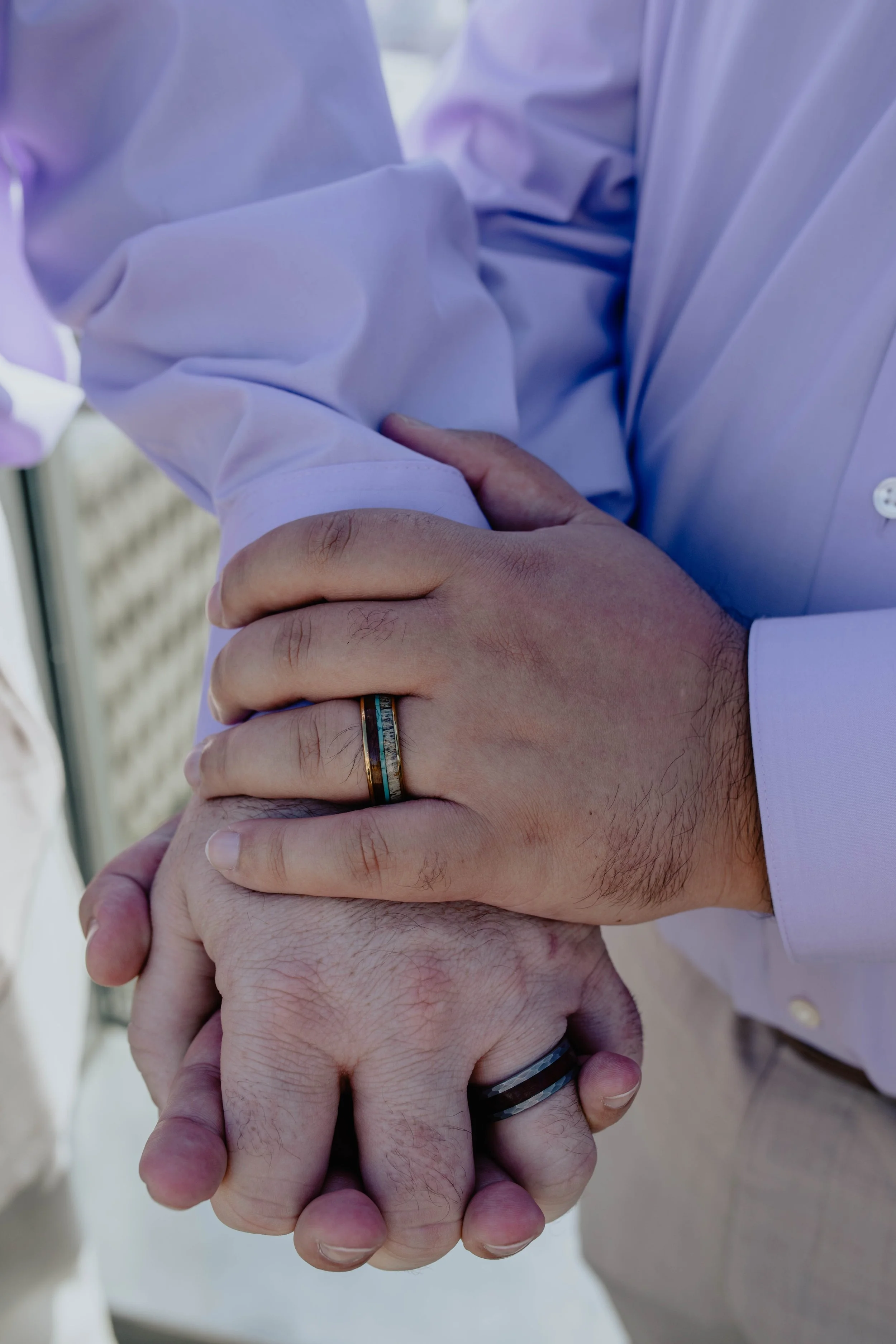 Two people holding hands, wearing matching wedding rings, with one person's arm resting on the other's arm, dressed in a light purple shirt. Seattle Municipal Courthouse wedding photography.