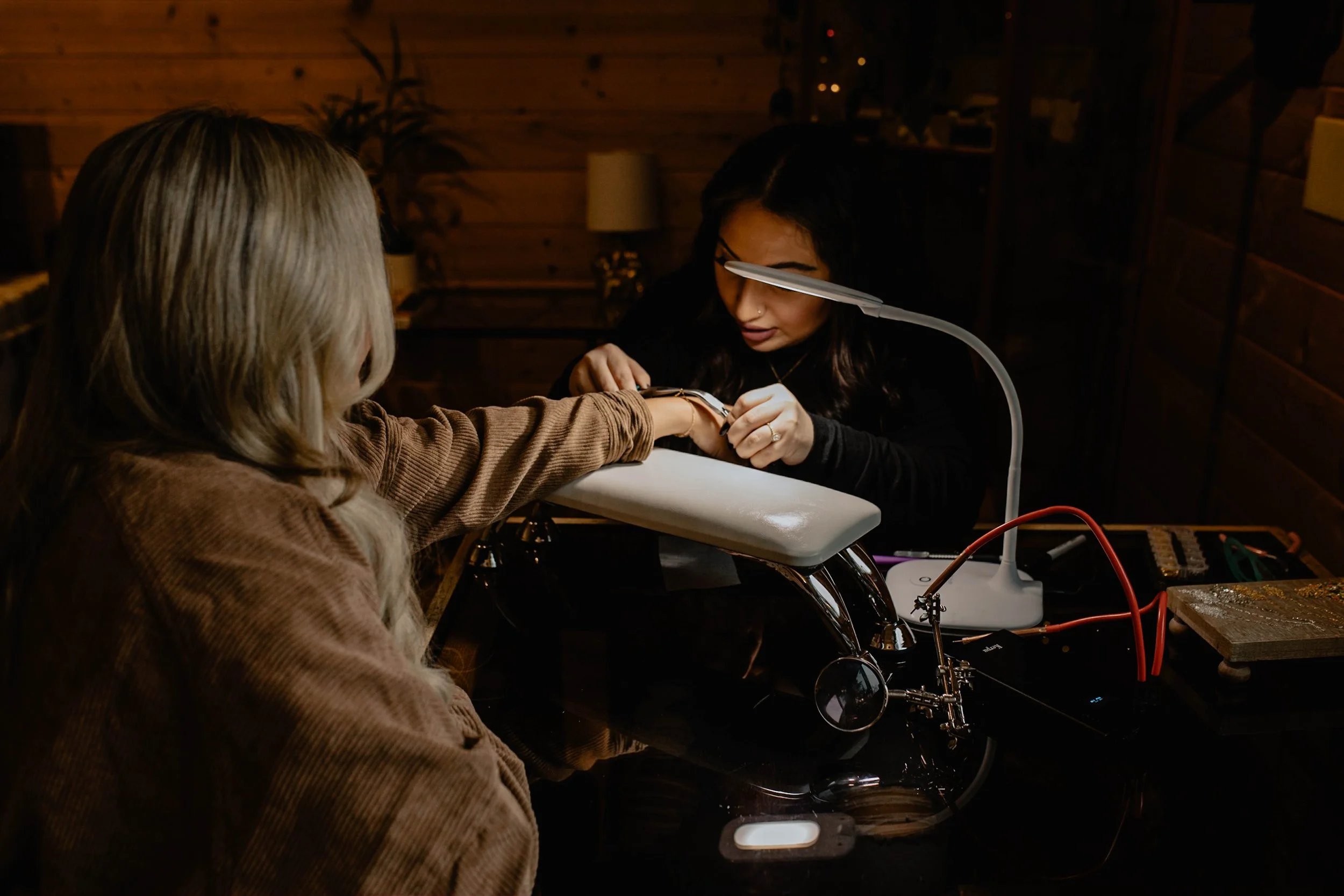 A woman getting a manicure from a technician in a salon with wooden walls, a desk lamp, and various tools on the table. Seattle professional head shot photography