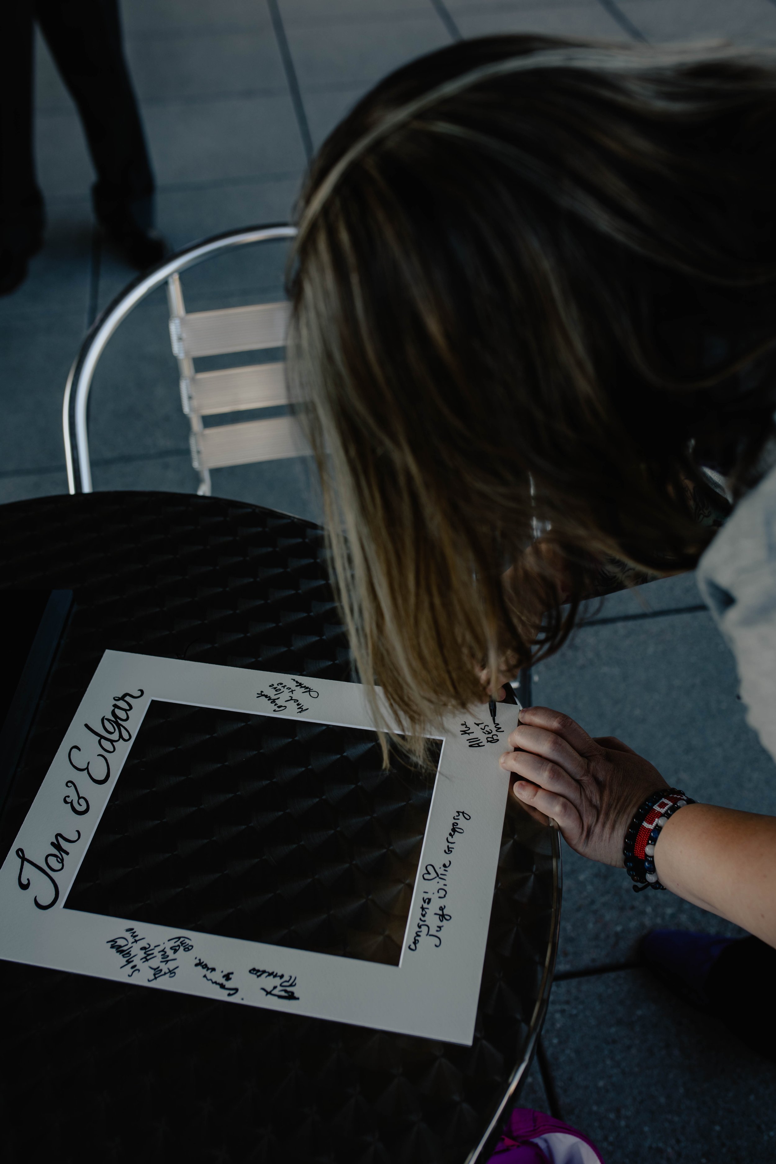 A person with brown hair signing a picture frame with handwritten notes on a black table. Seattle Municipal Courthouse wedding photography.
