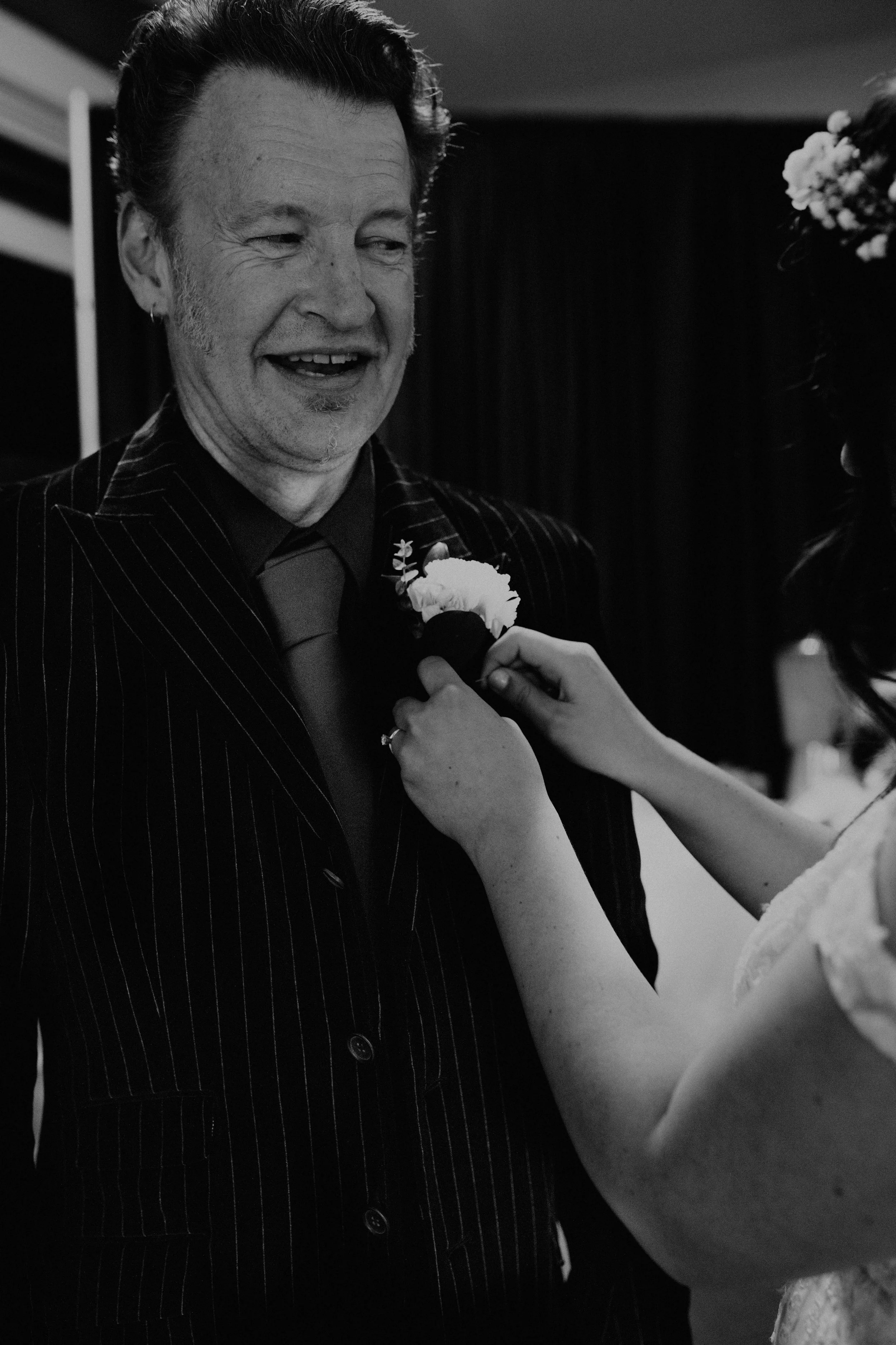 A woman pins a flower boutonniere onto a man's lapel at a wedding or formal event. Seattle, WA wedding photography.