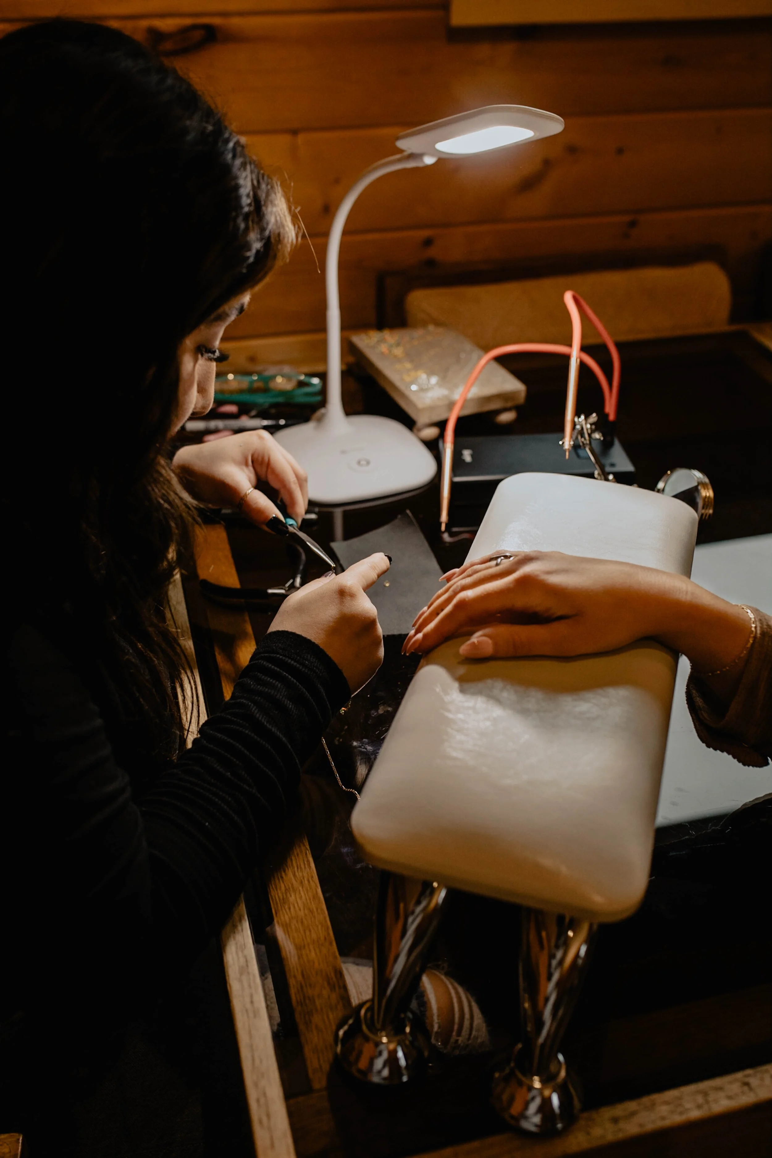 A person receiving a manicure at a nail salon, with a technician applying nail polish or a nail treatment to a client's fingernails. The scene includes a work lamp, tools, and nail supplies on the table. Seattle professional head shot photography