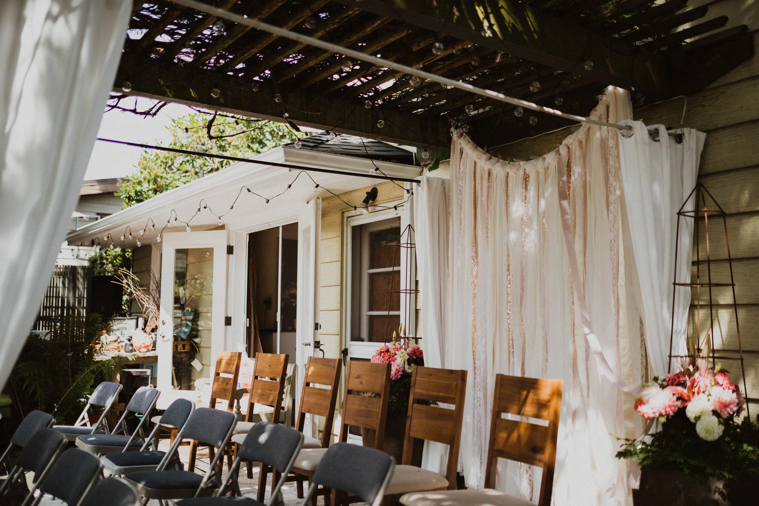Outdoor wedding or event setup with chairs, decorative drapes, flowers, and string lights under a wooden pergola. Seattle, WA wedding photography.
