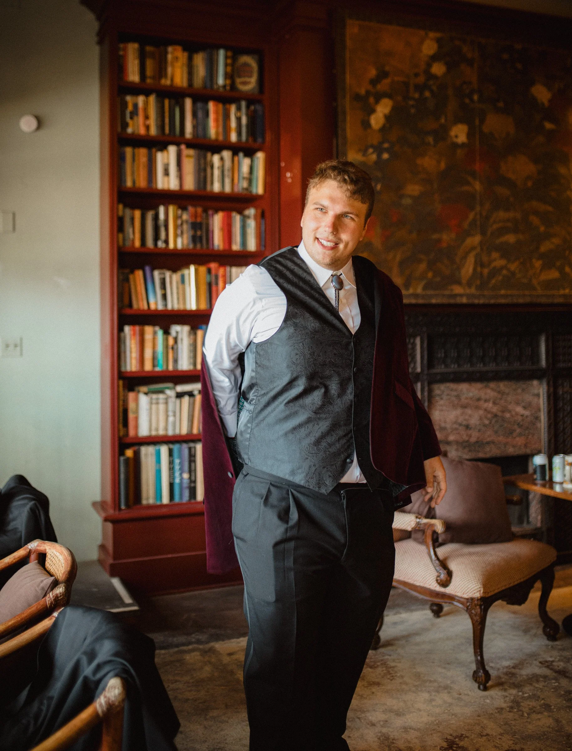 Groom puts on his suit jacket in the getting ready library of the The Ruins wedding venue in Queen Anne, Seattle