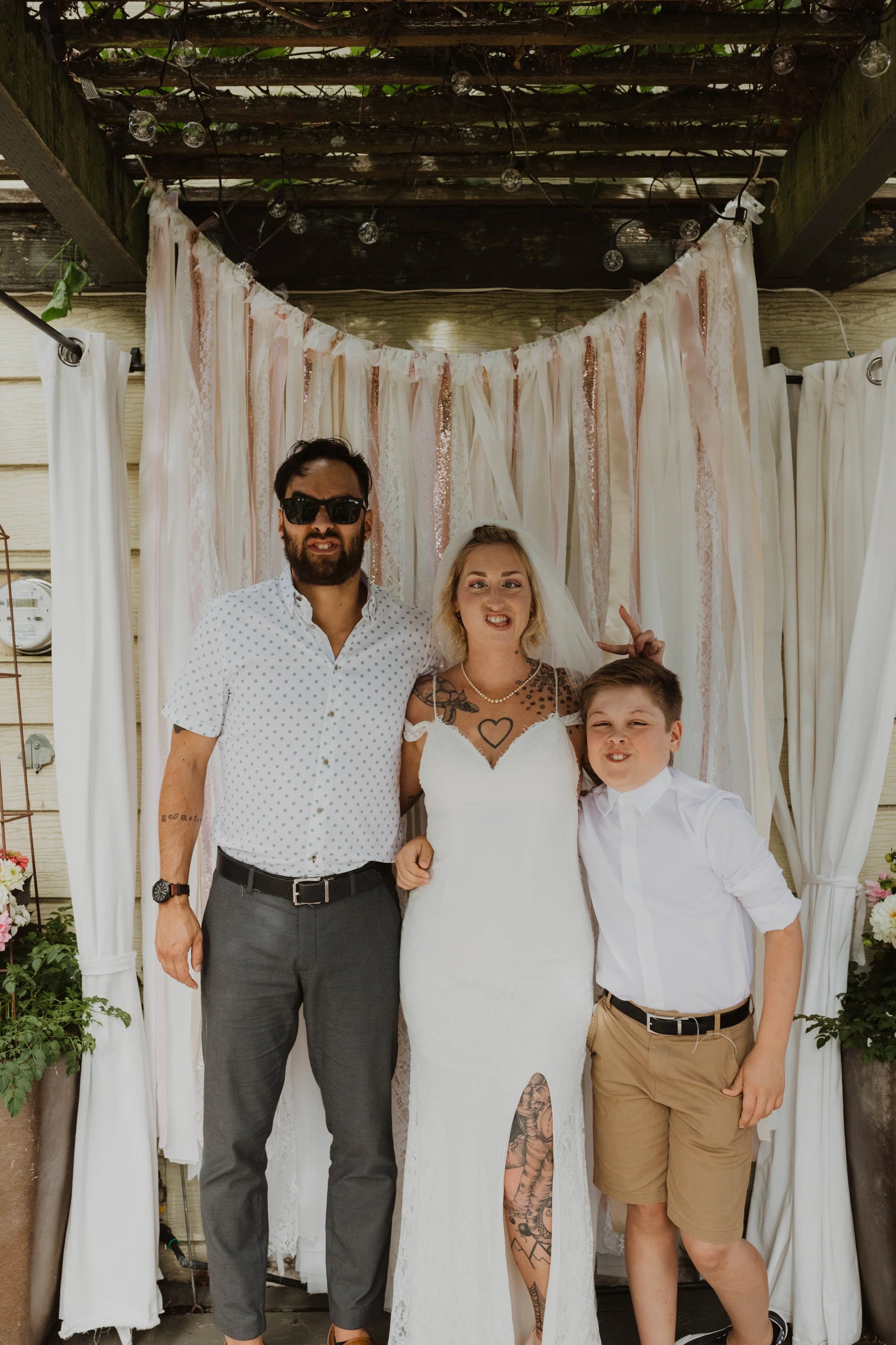 A group of three people standing in front of a decorated backdrop at a wedding, with a man, a woman, and a young boy making silly faces. Seattle, WA wedding photography.