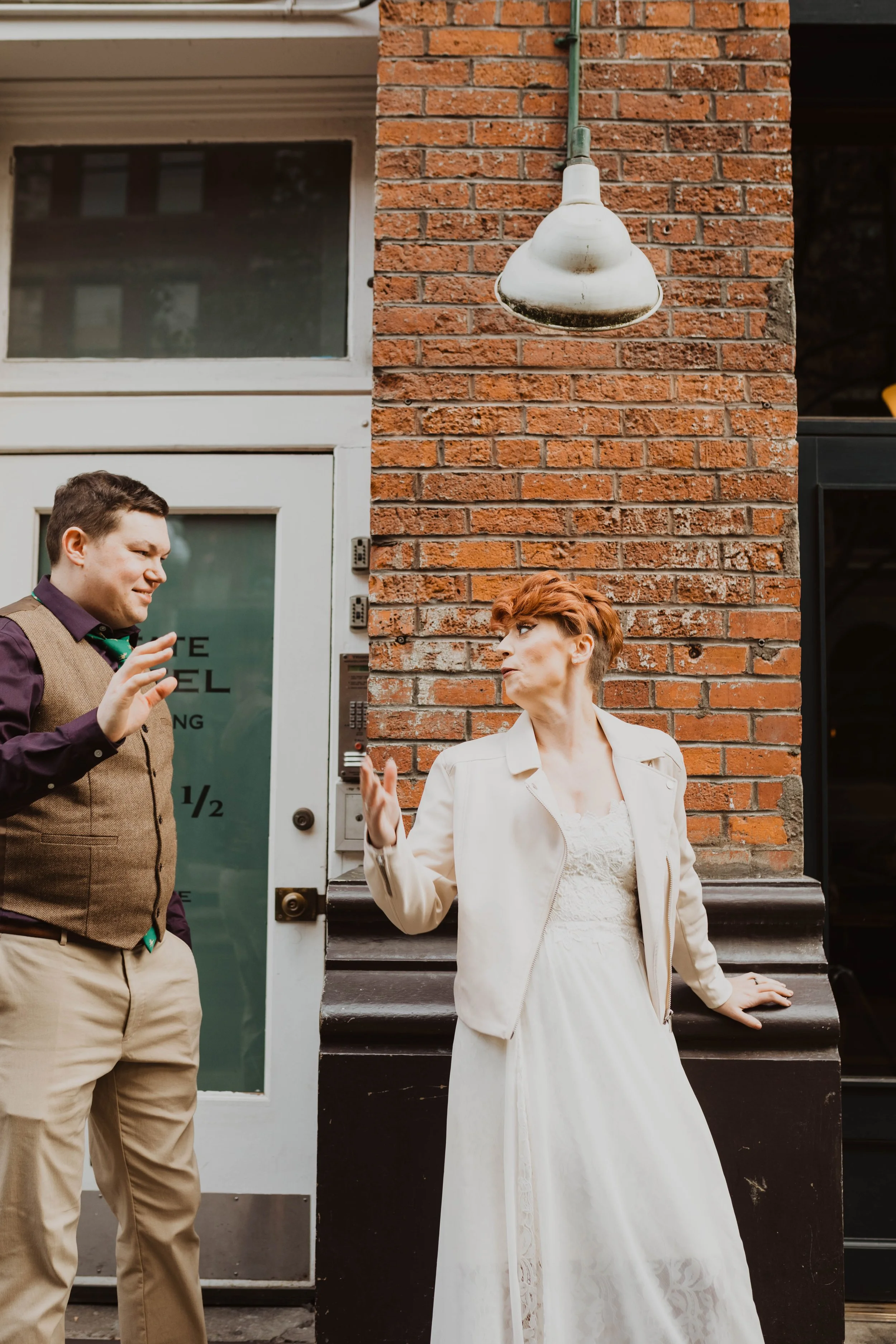 A man and a woman standing outside a brick building, engaging in a conversation or disagreement, with the woman leaning against a black ledge and the man gesturing with his right hand. Pioneer Square, Seattle, WA wedding photography.