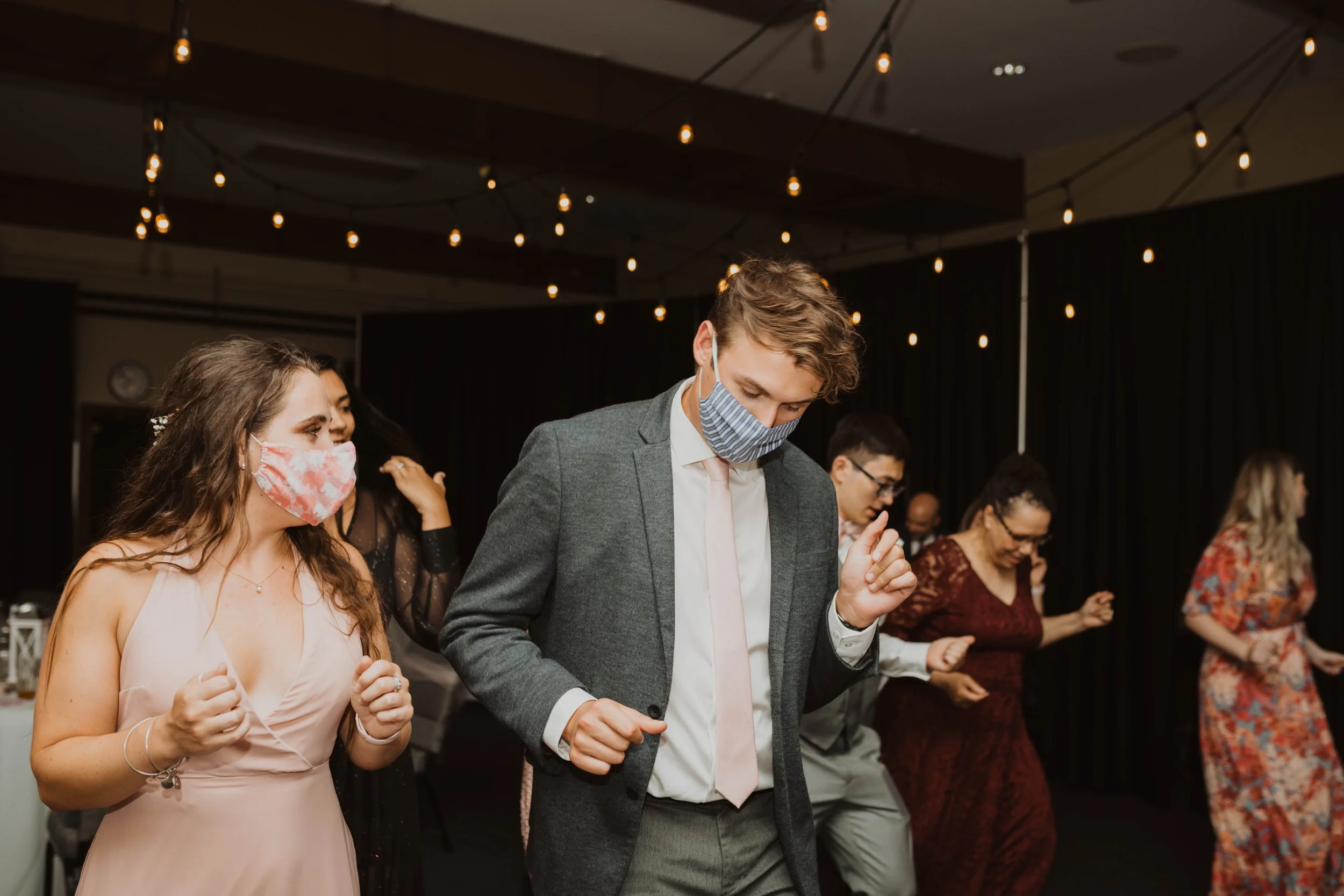 People dancing at a party or event, wearing face masks, with string lights hanging overhead. Seattle, WA wedding photography.
