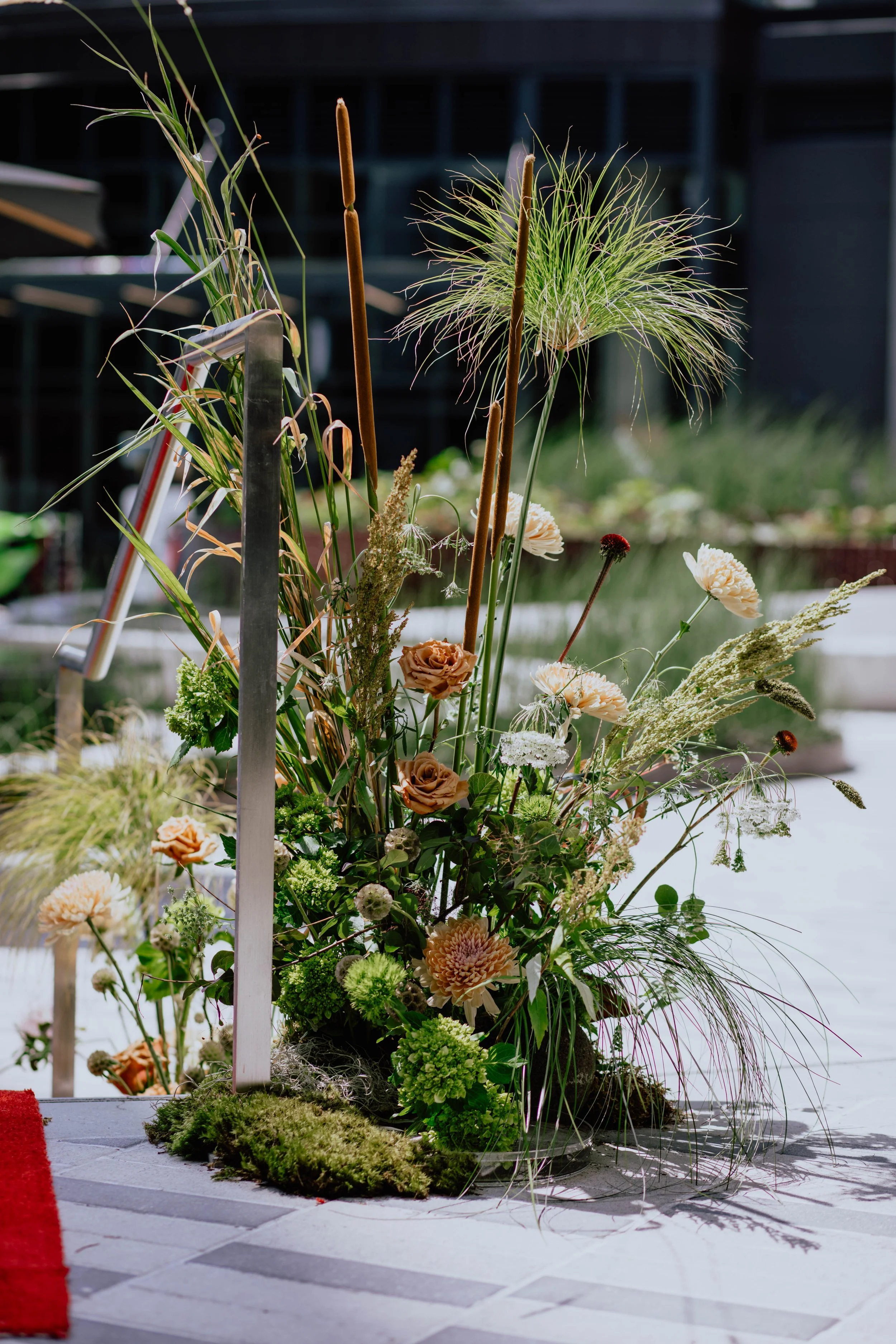 A floral arrangement with various green and beige flowers and tall grasses, placed on a tiled surface outdoors. Seattle event photography