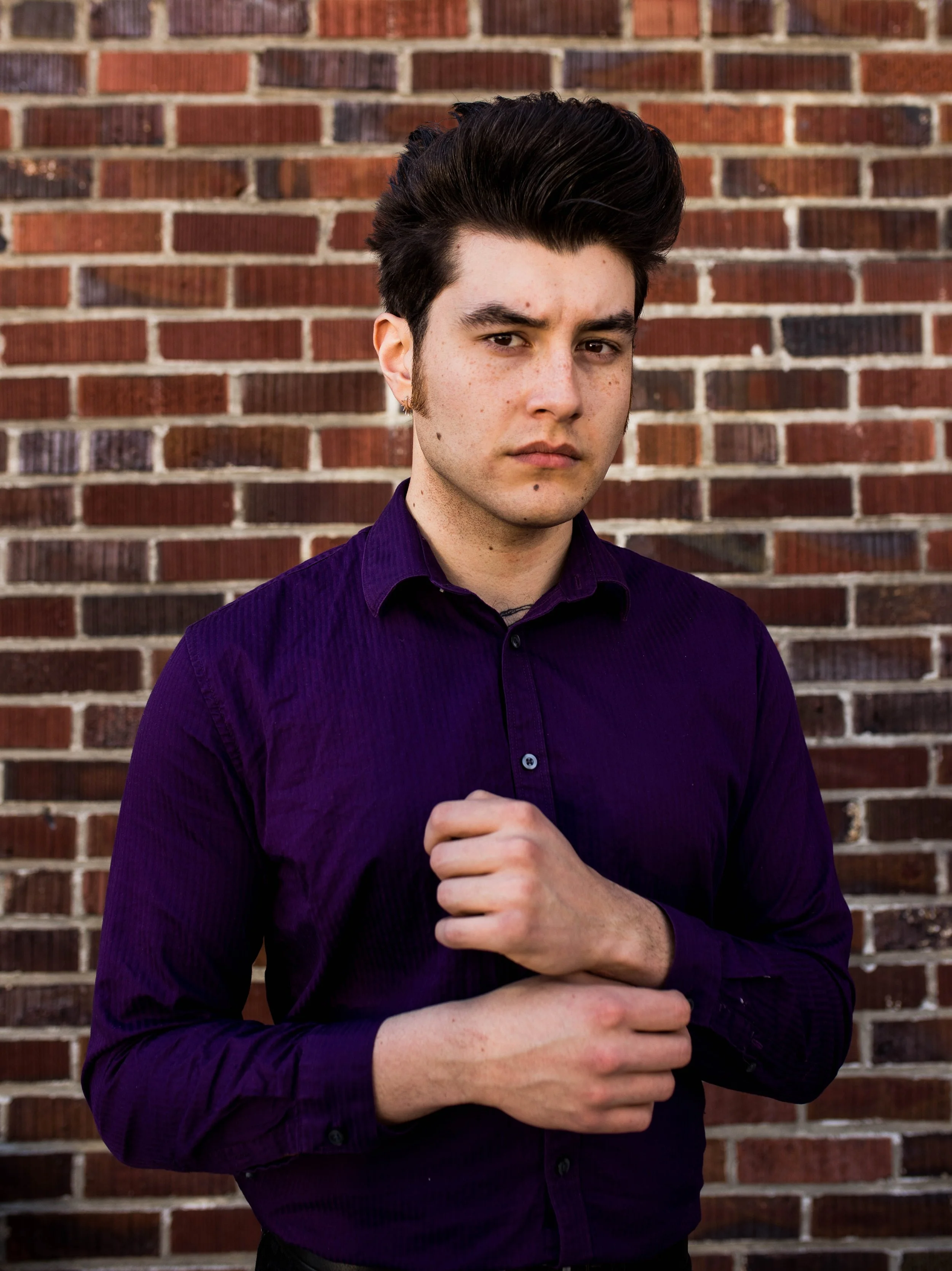 Young man with dark hair, wearing a dark purple shirt, standing in front of a brick wall. Seattle professional head shot photography