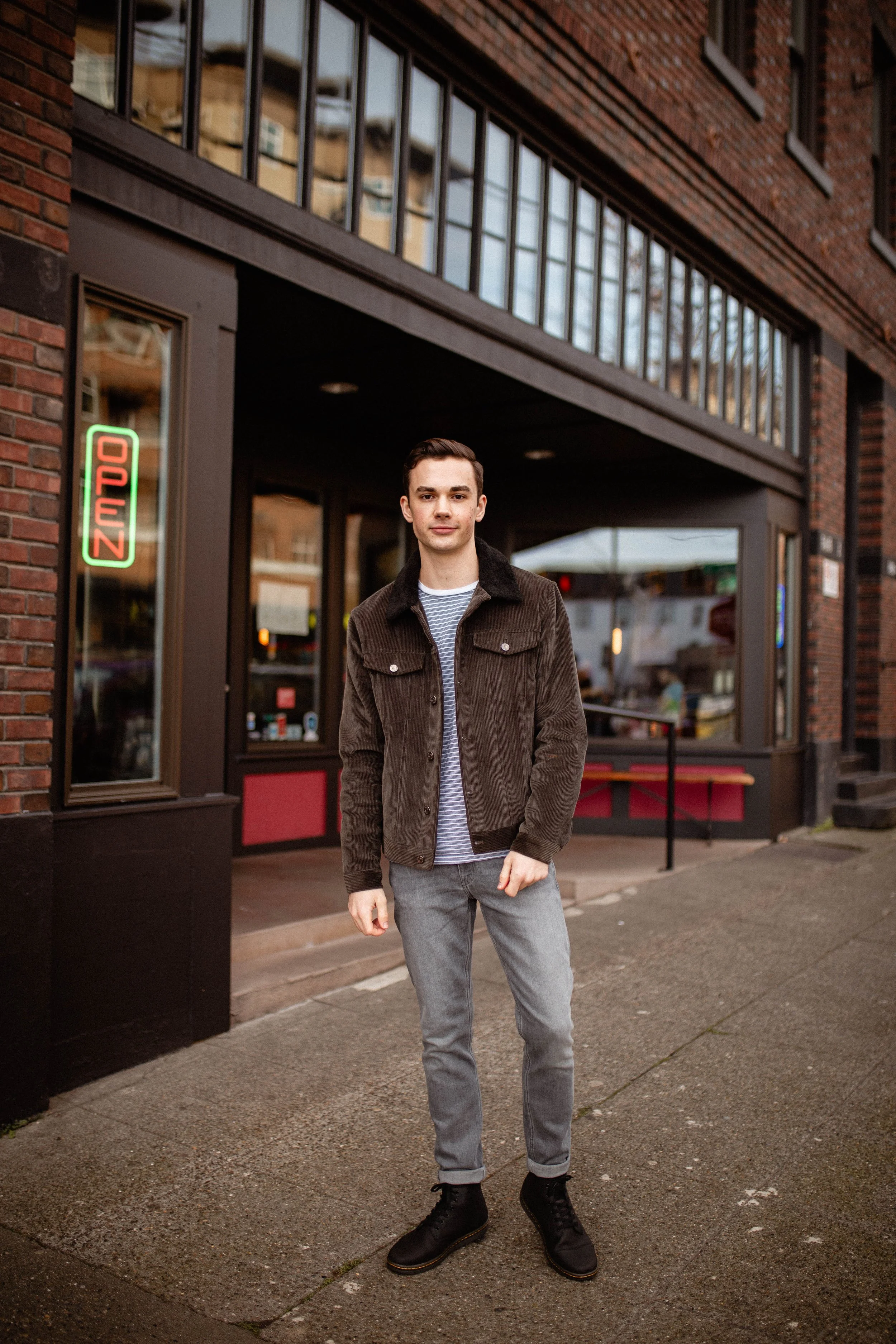 A young man standing outside a restaurant with an illuminated 'Open' sign in the window. Seattle professional head shot photography