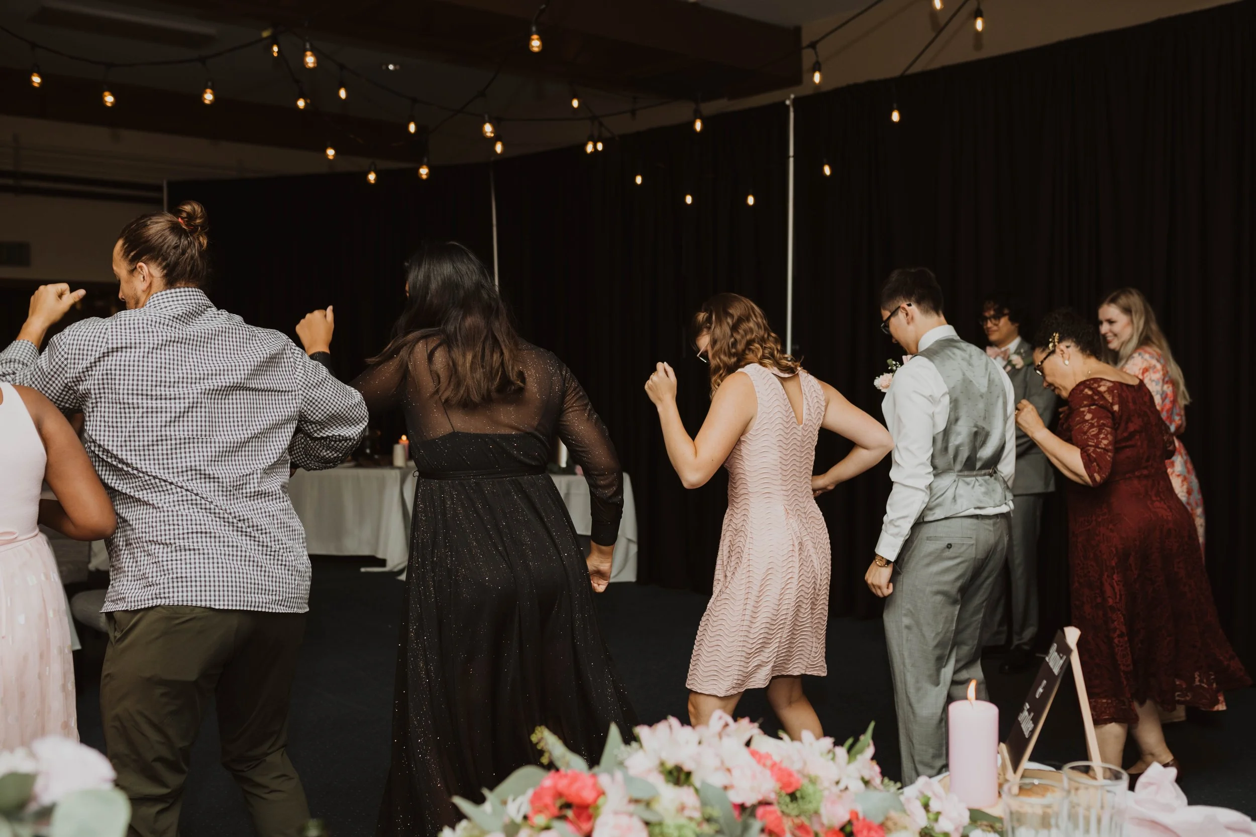 People dancing at a wedding reception under string lights with a dark curtain backdrop. Seattle, WA wedding photography.