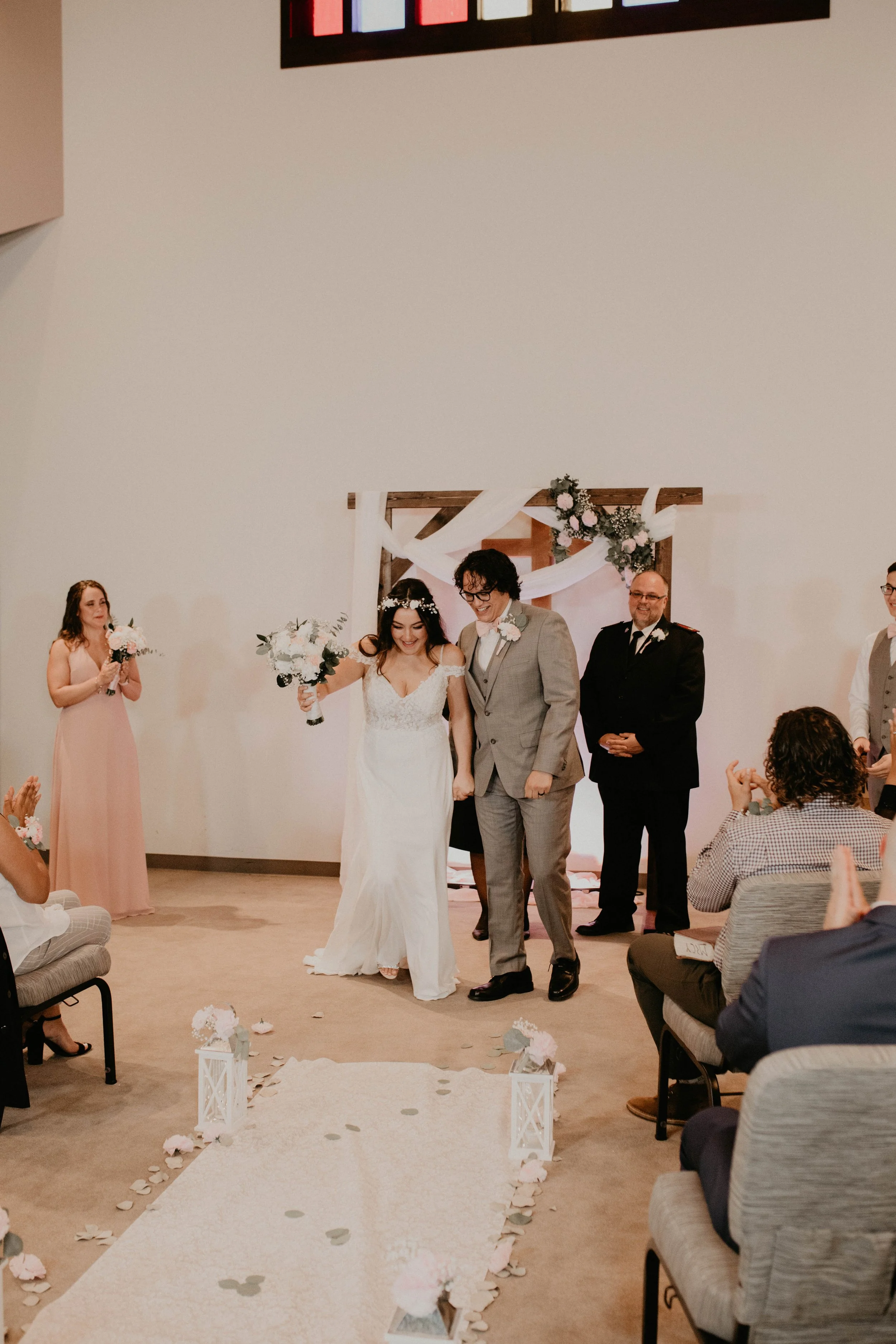 A bride and groom walking down the aisle after their wedding ceremony, surrounded by seated guests and bridal party members, with floral decorations. Seattle, WA wedding photography.
