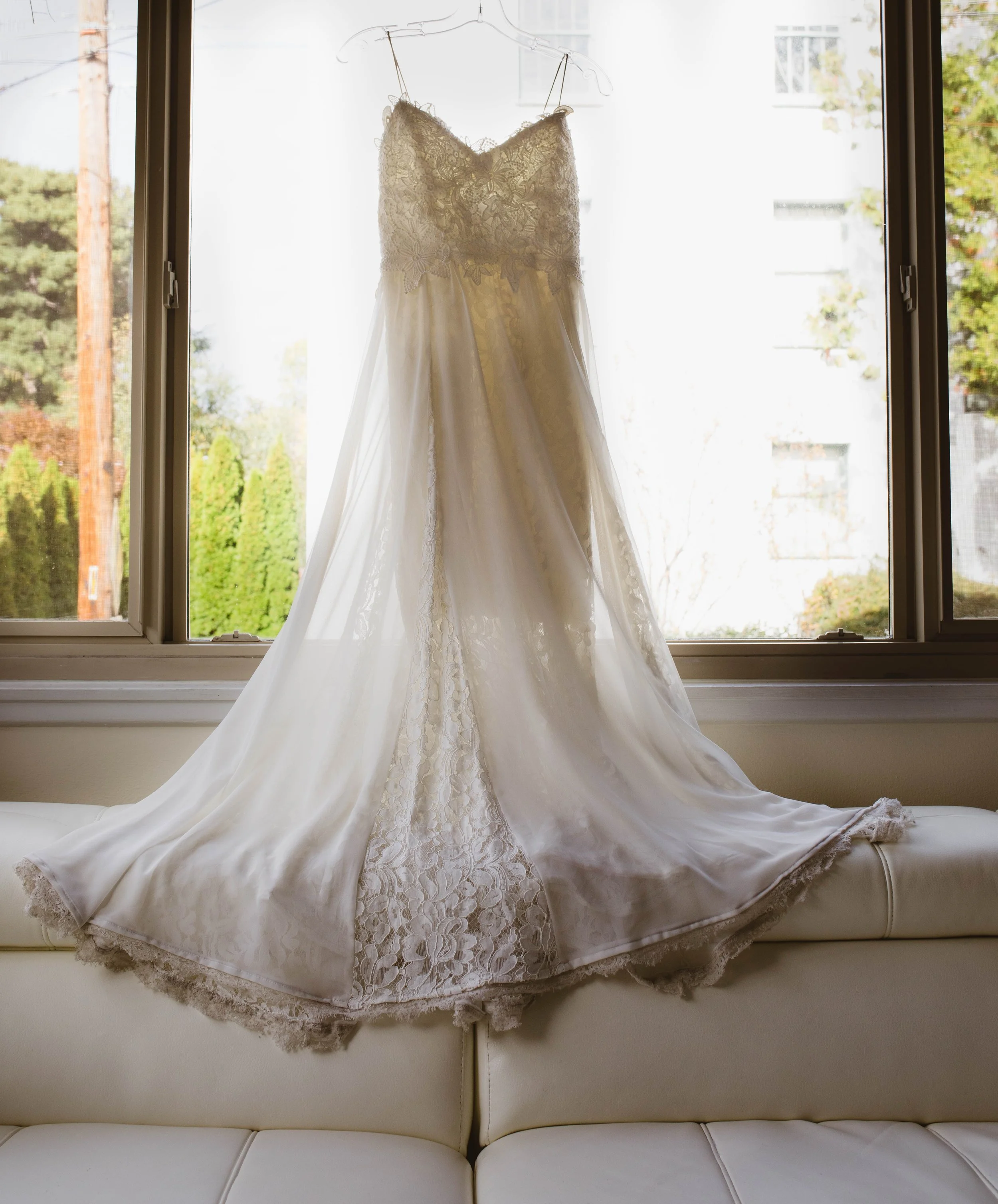 White wedding dress hanging on a hanger in front of a window. Pioneer Square, Seattle, WA wedding photography.