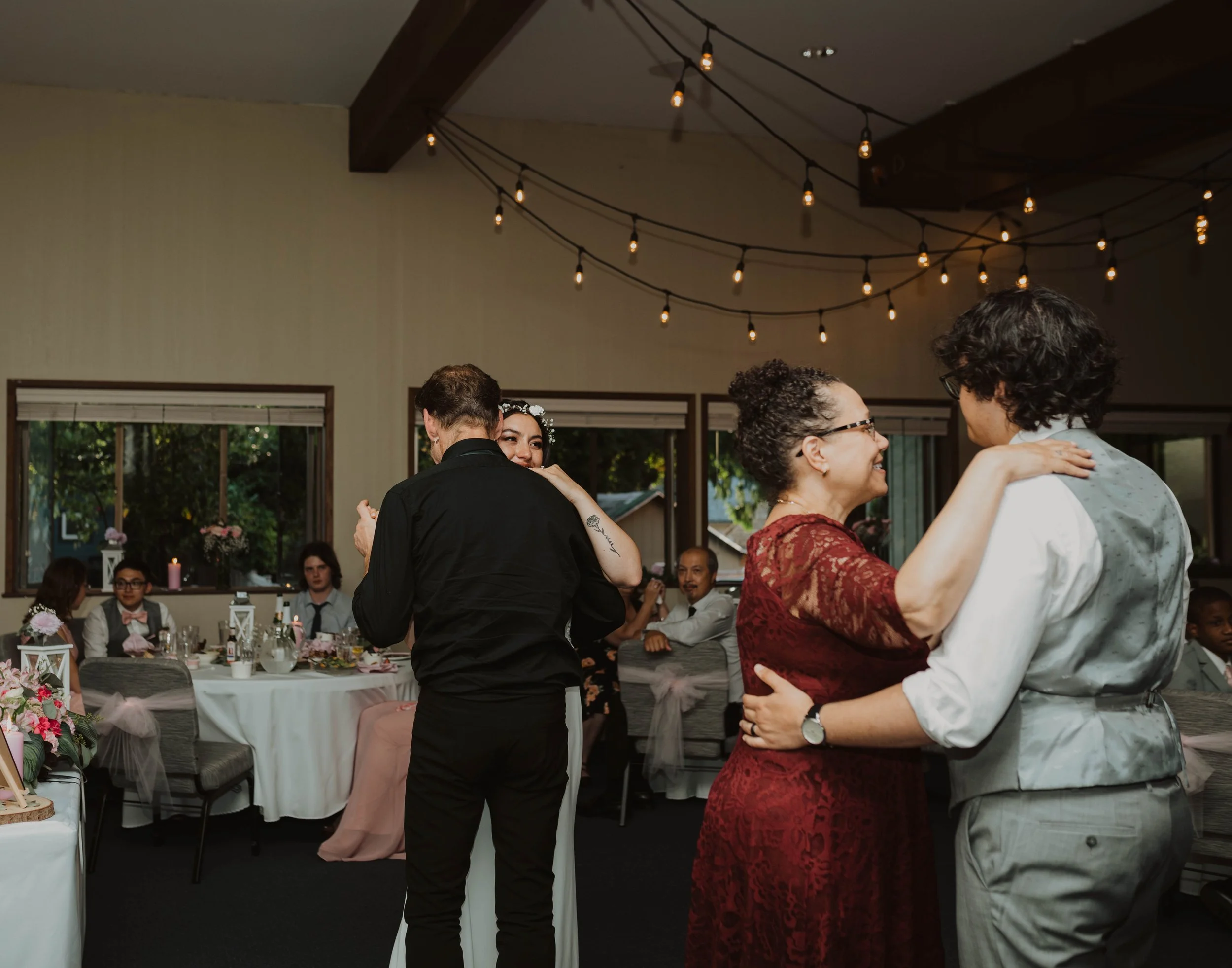 People dancing at a wedding reception in a decorated indoor venue with string lights, tables, and floral centerpieces. Seattle, WA wedding photography.