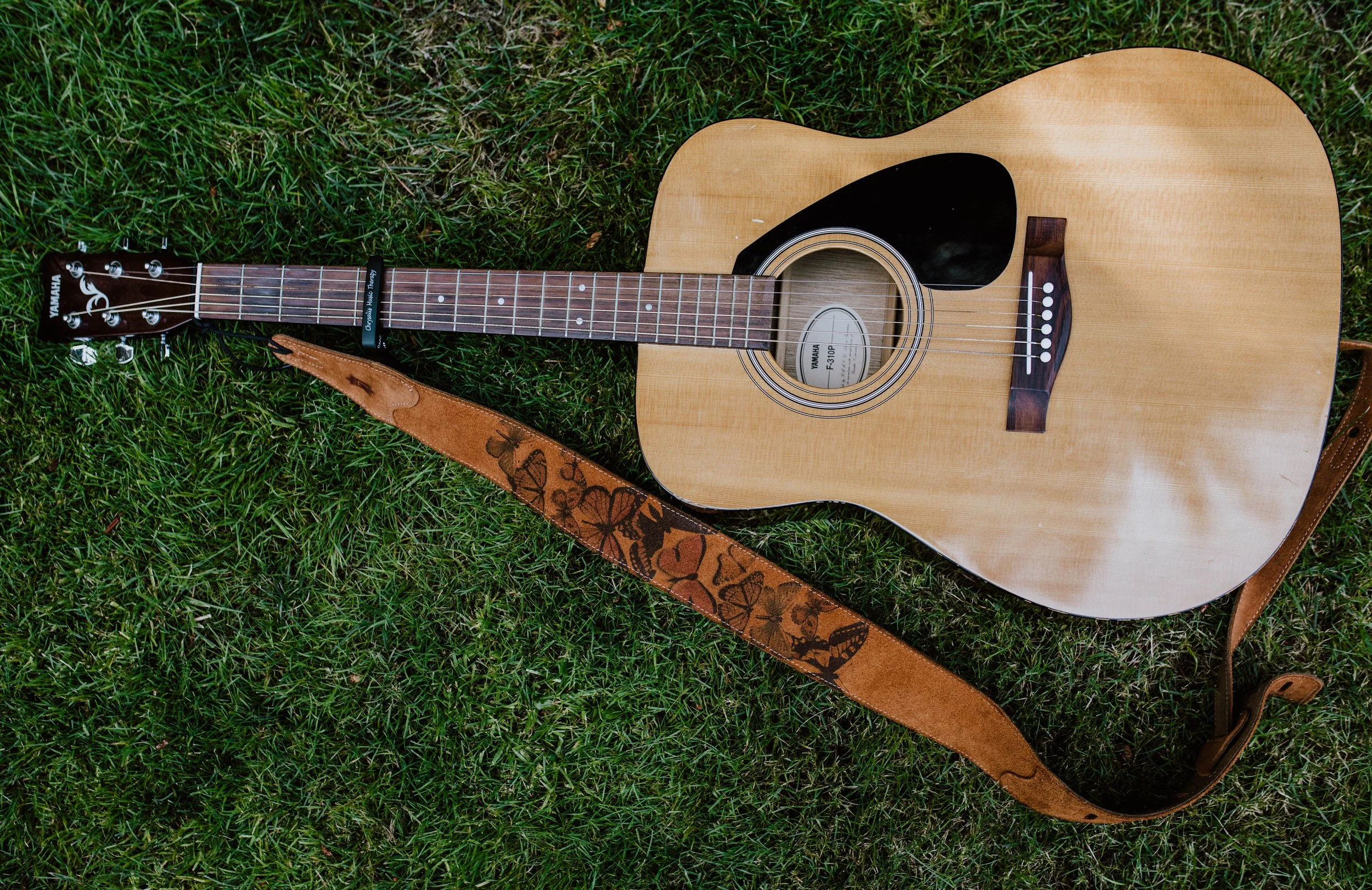 An acoustic Yamaha guitar with a butterfly-shaped strap lying on green grass. Seattle professional head shot photography