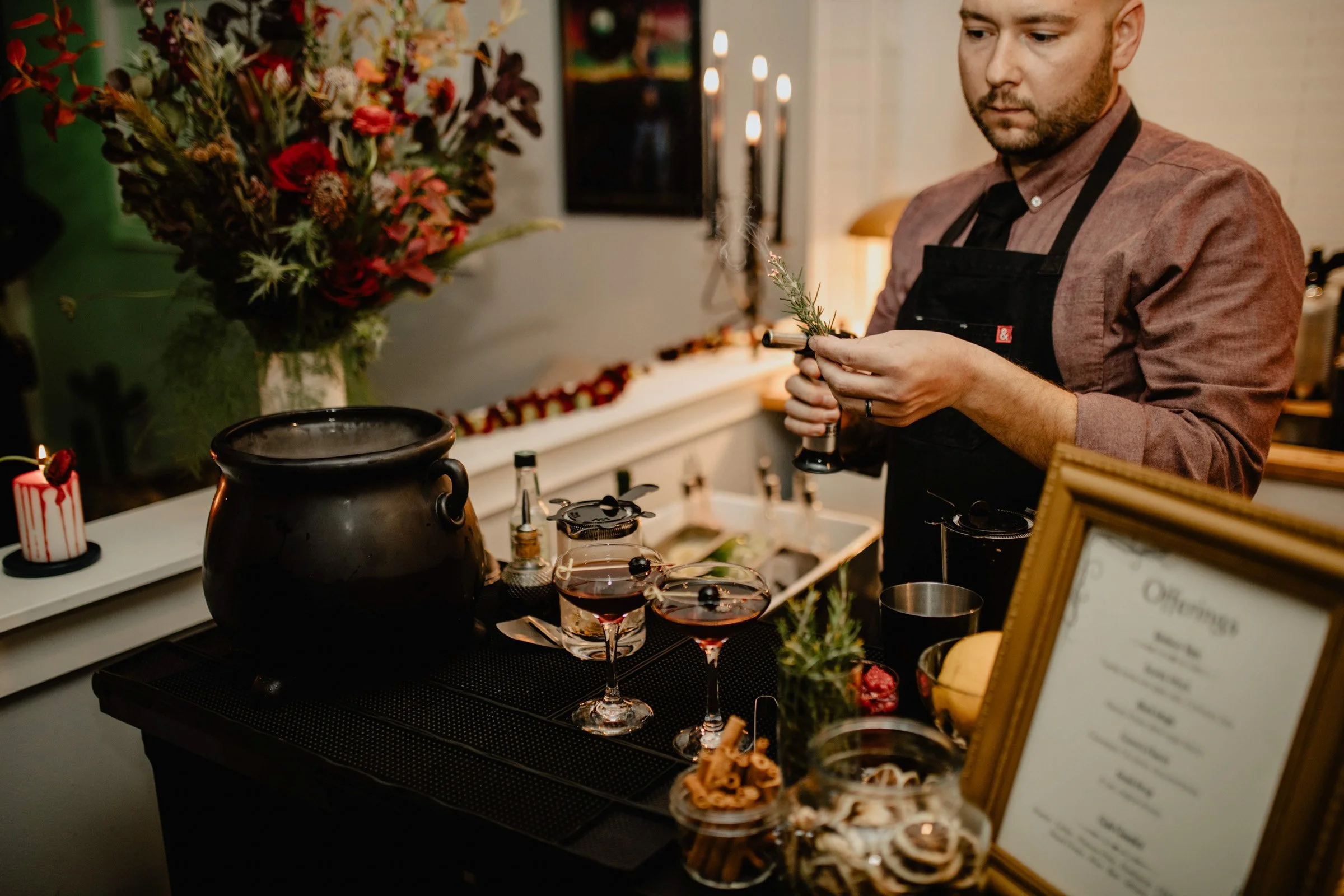 Bartender adds flair to his cocktails by torching a garnish of rosemary for this Halloween weekend wedding in Seattle