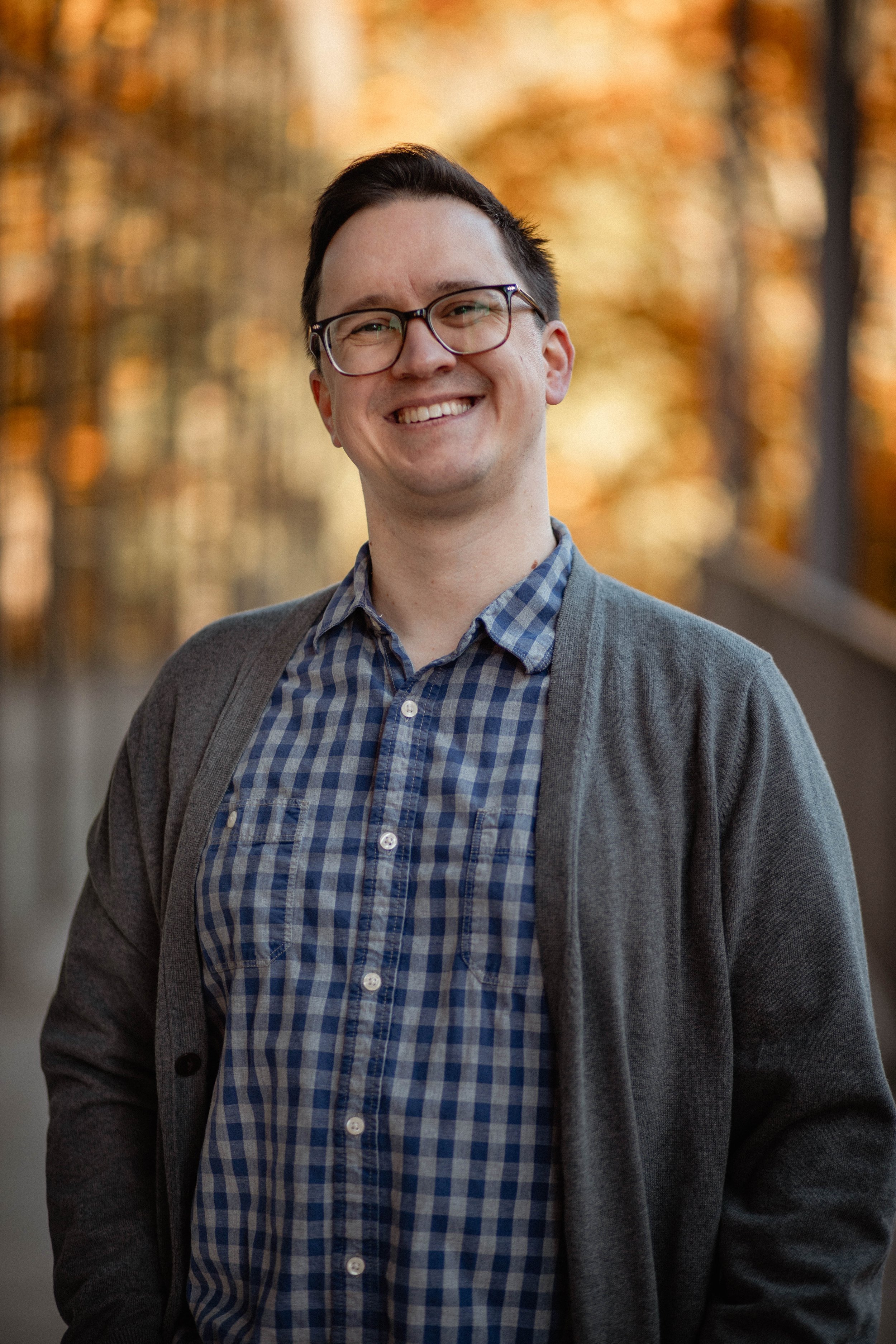 Smiling man with glasses, wearing a checkered shirt and gray cardigan outdoors during autumn. Seattle professional head shot photography