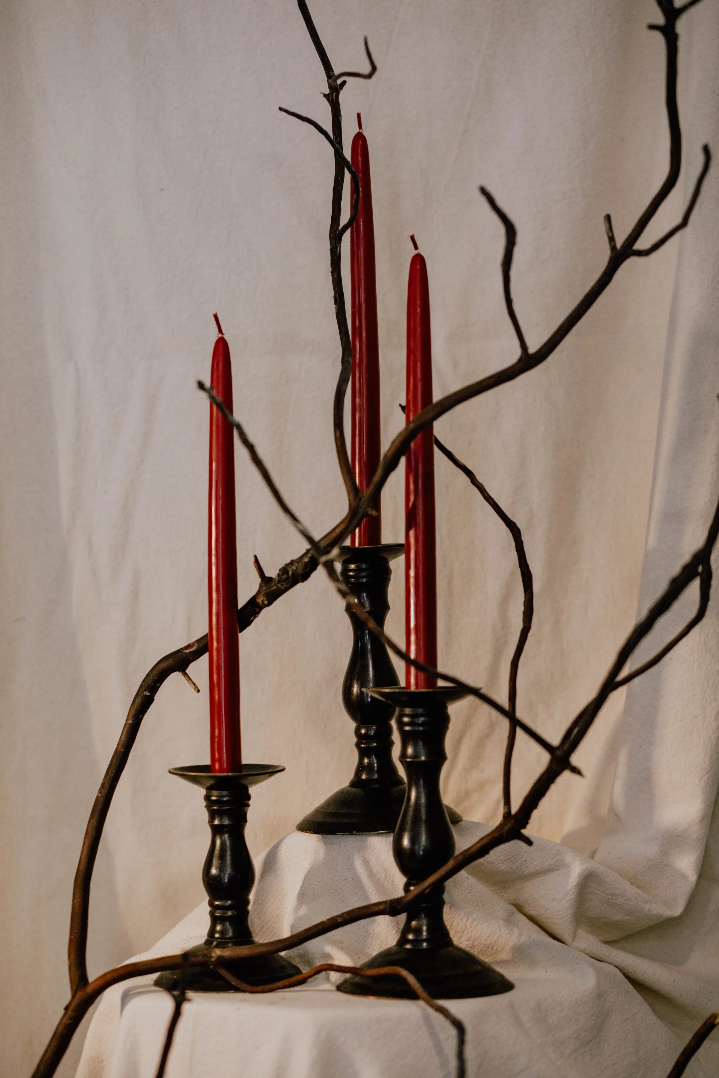 Three black candlesticks with red candles on a white cloth, with leafless twigs arranged around them.  Seattle product photography