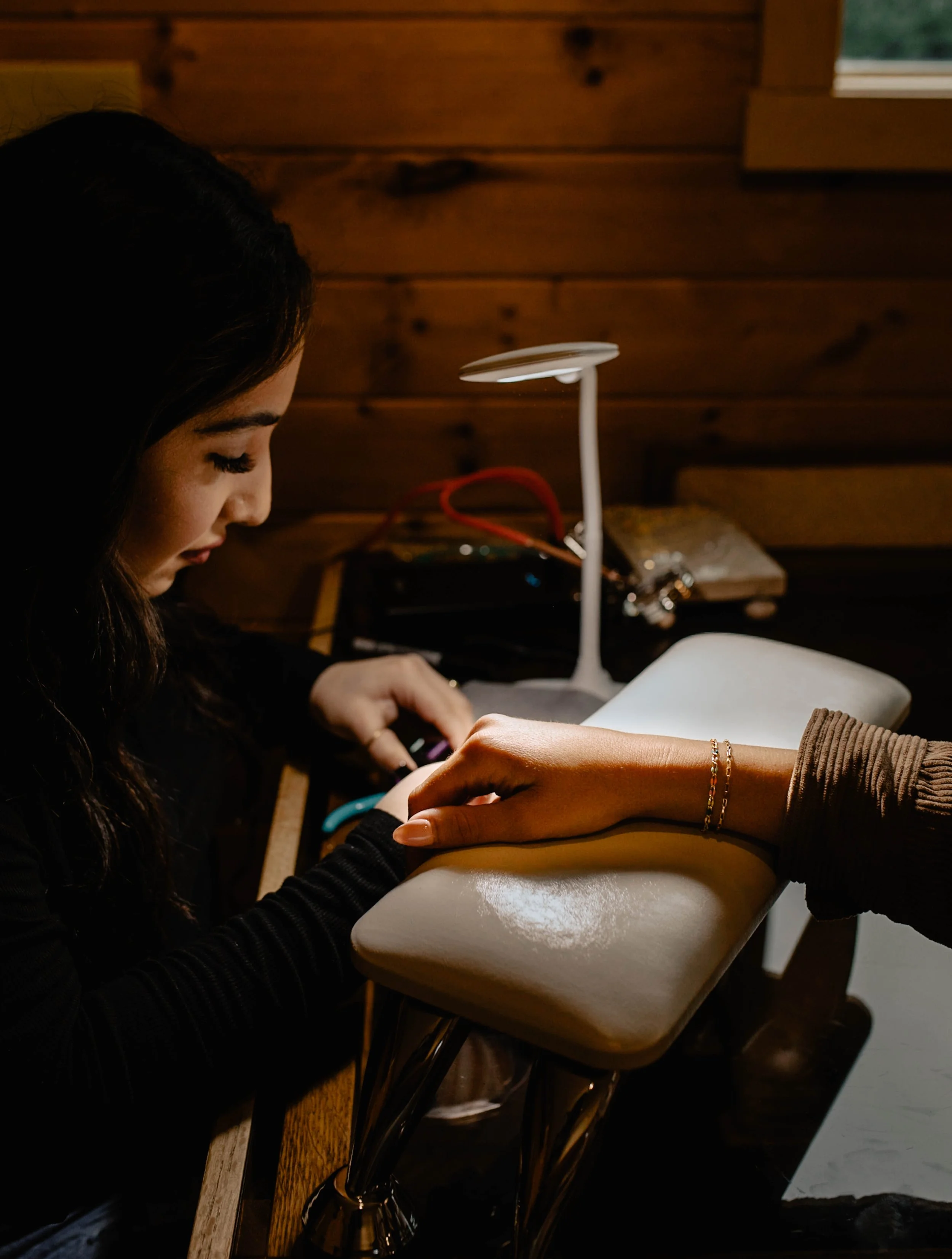 A woman getting a manicure at a nail salon, with a focused expression, seated at a table with a lamp and manicure tools. Seattle professional head shot photography
