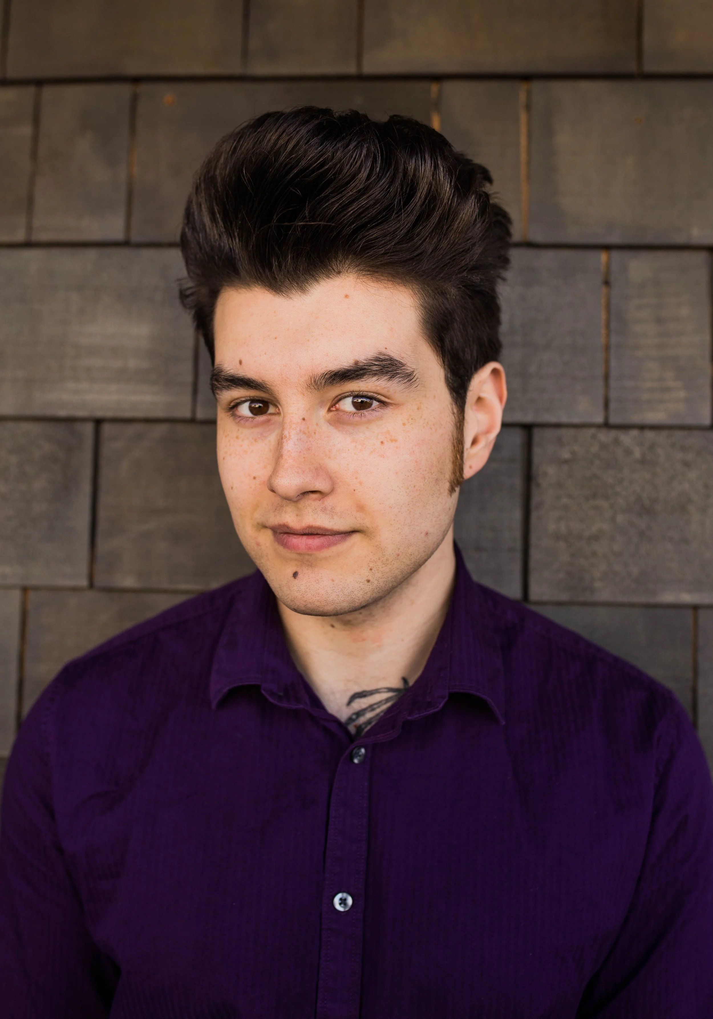A young man with dark hair, wearing a purple shirt, standing against a wooden wall background. Seattle professional head shot photography