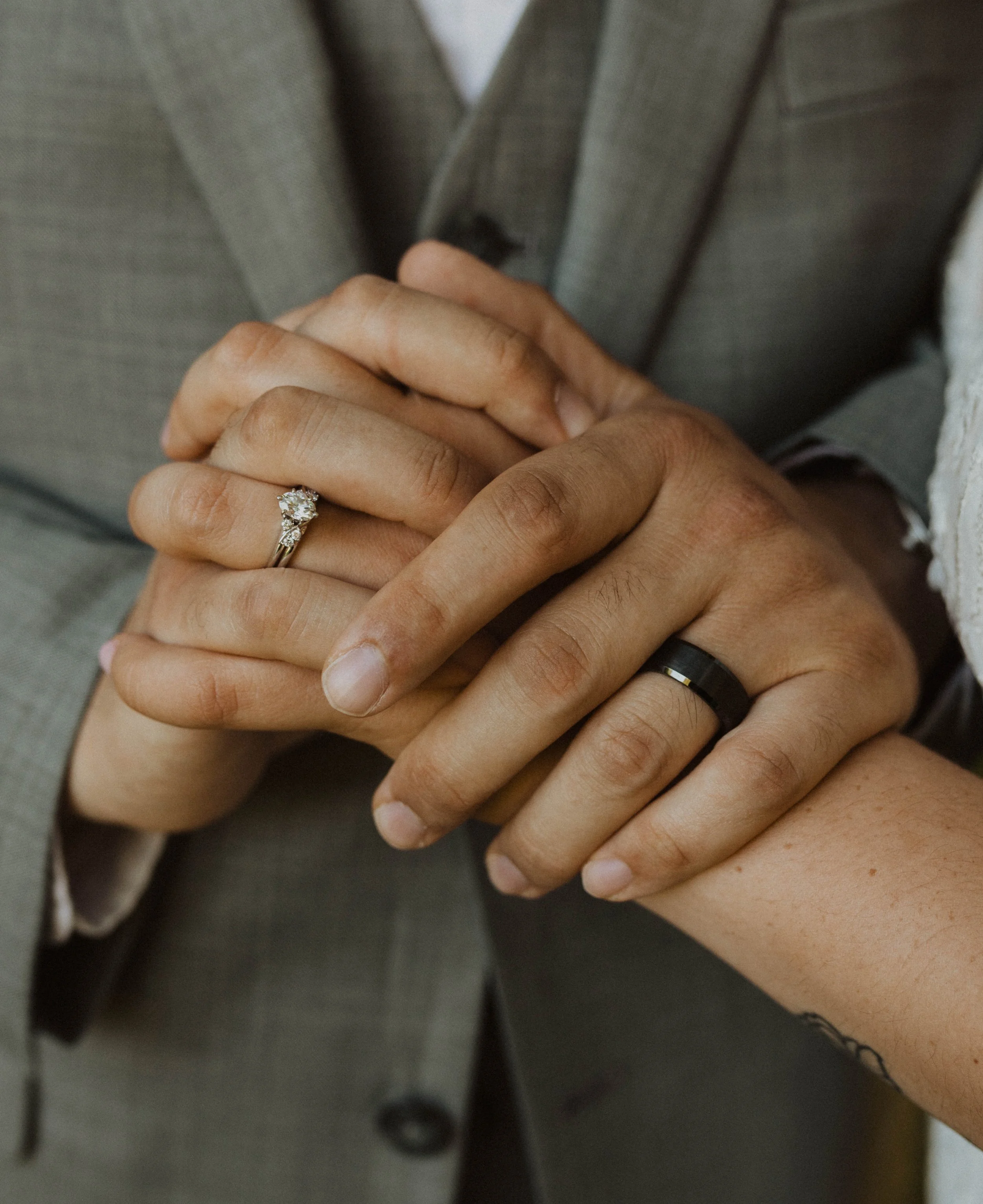 A close-up of a couple holding hands, wearing wedding rings, with a man in a gray suit and a woman with a tattoo on her wrist. Seattle, WA wedding photography.