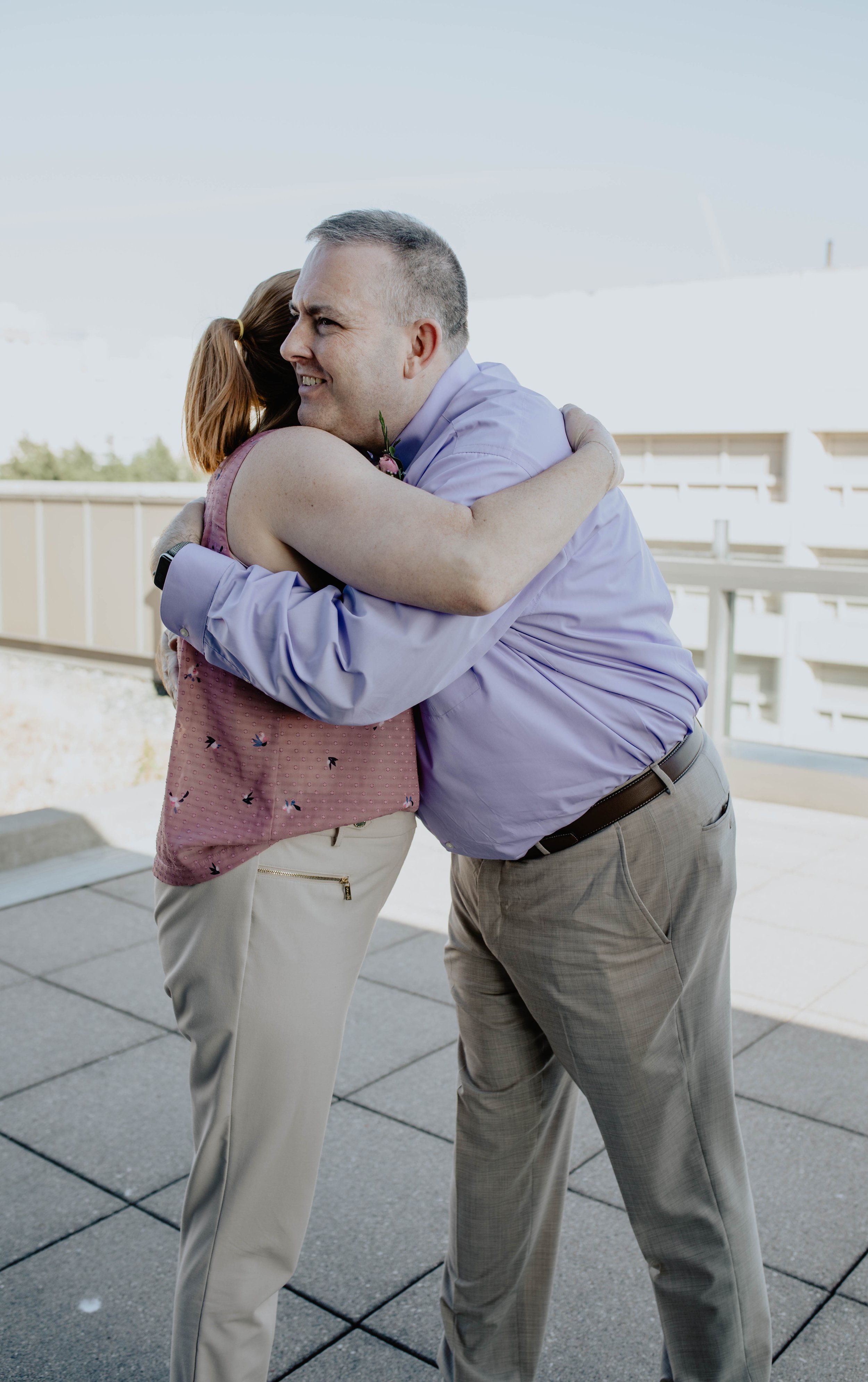 Two people hugging outdoors, a man and a woman, with the man smiling broadly. Seattle Municipal Courthouse wedding photography.
