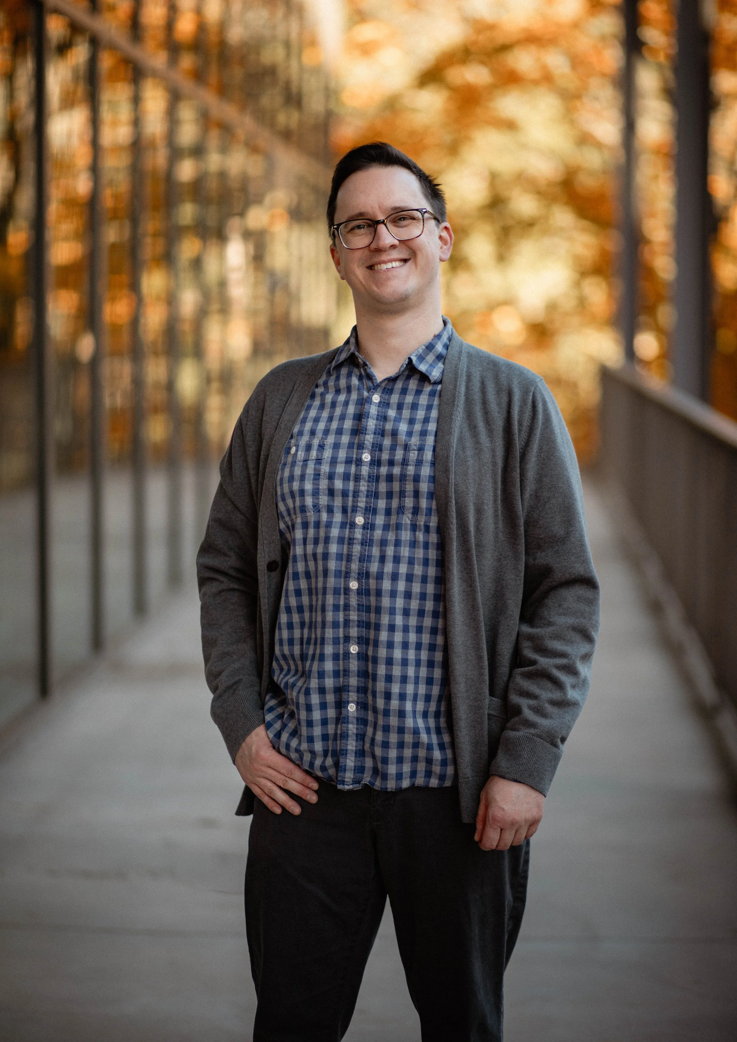 A smiling man with glasses standing on a bridge with fall foliage in the background. Seattle professional head shot photography
