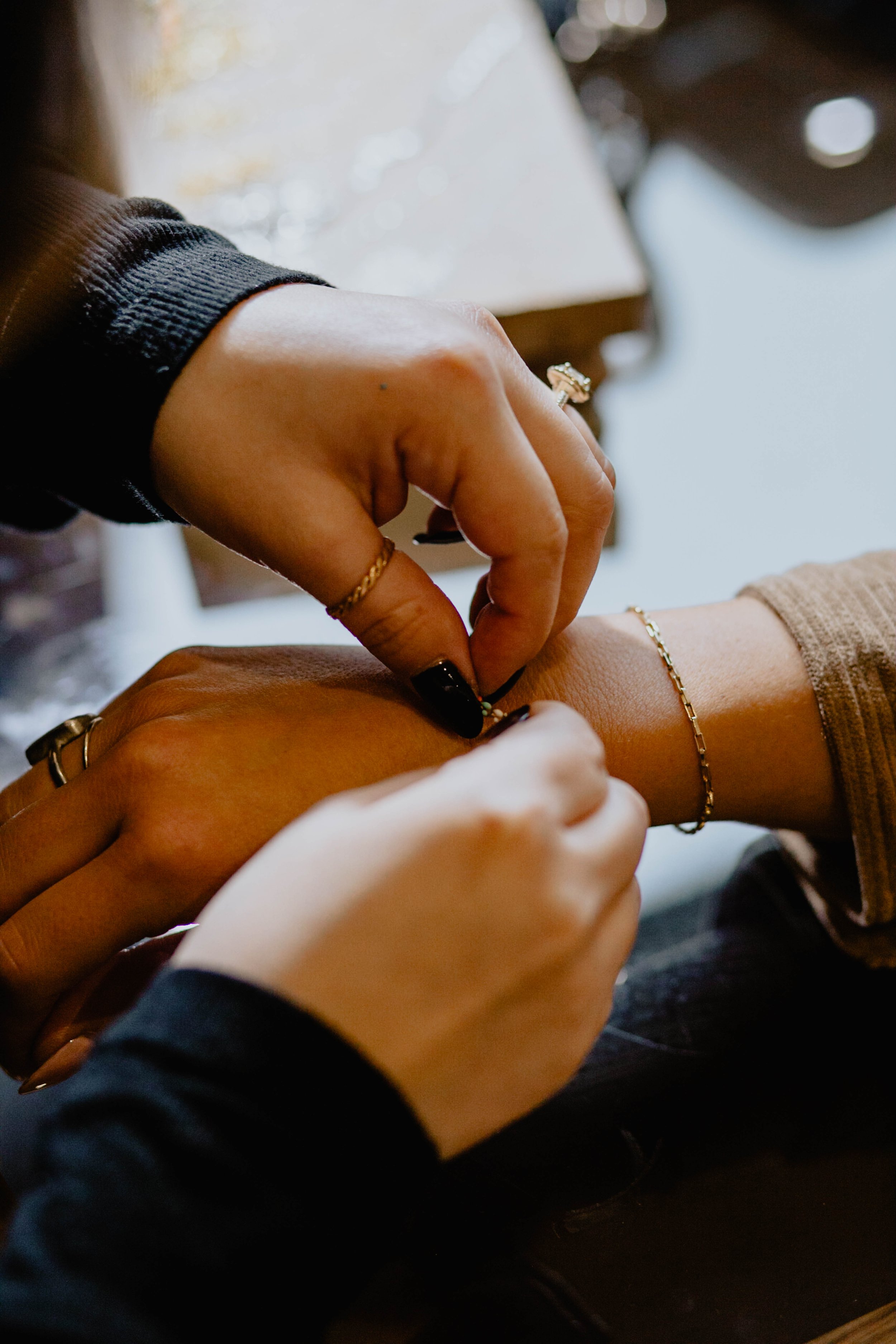 Two people are exchanging jewelry, with one person placing a bracelet on the other's wrist. Both are wearing rings and bracelets, and one person has black nail polish. Seattle professional head shot photography