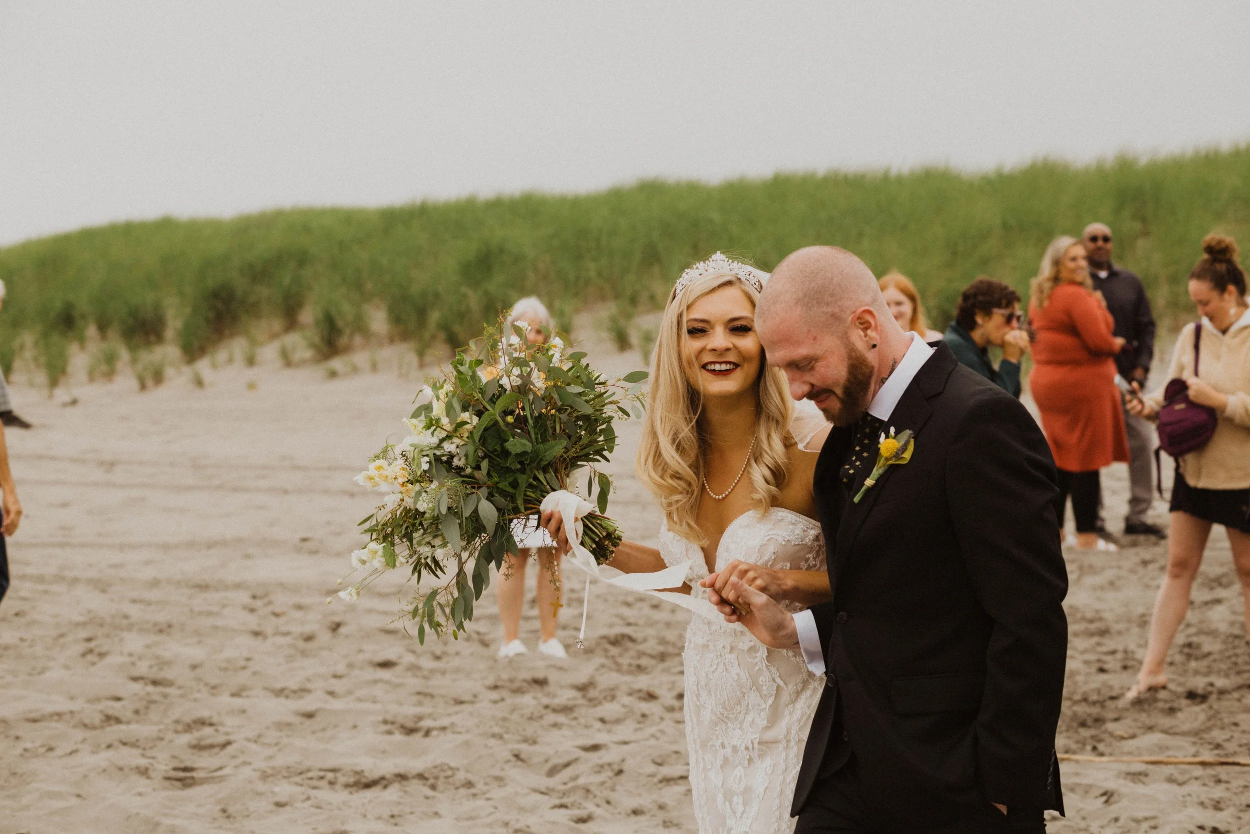 A bride and groom celebrating their wedding on a beach, with friends in the background. Long Beach, WA wedding photography.
