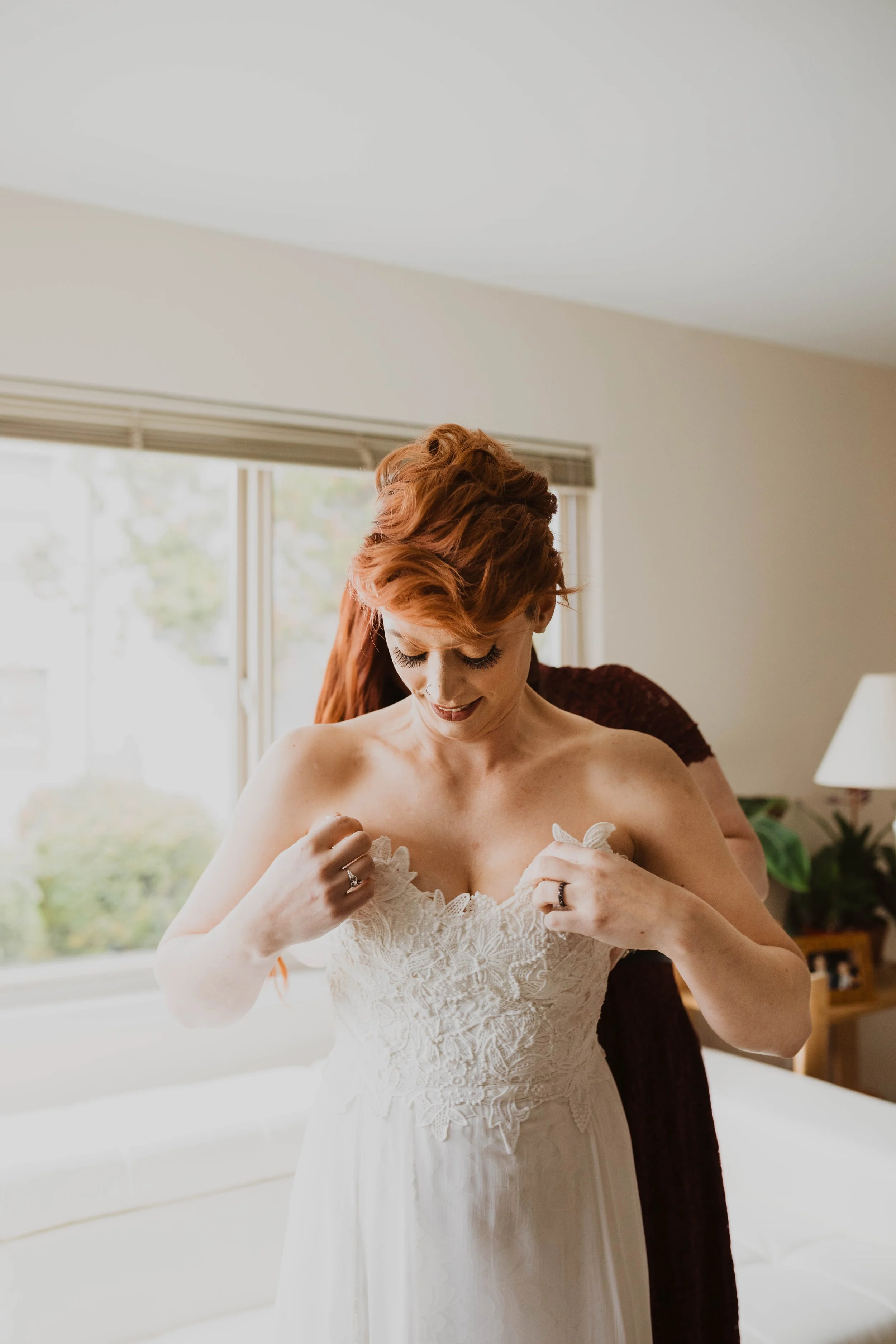 A bride with red hair adjusting her wedding dress inside a room with a large window and natural light.  Pioneer Square, Seattle, WA wedding photography.