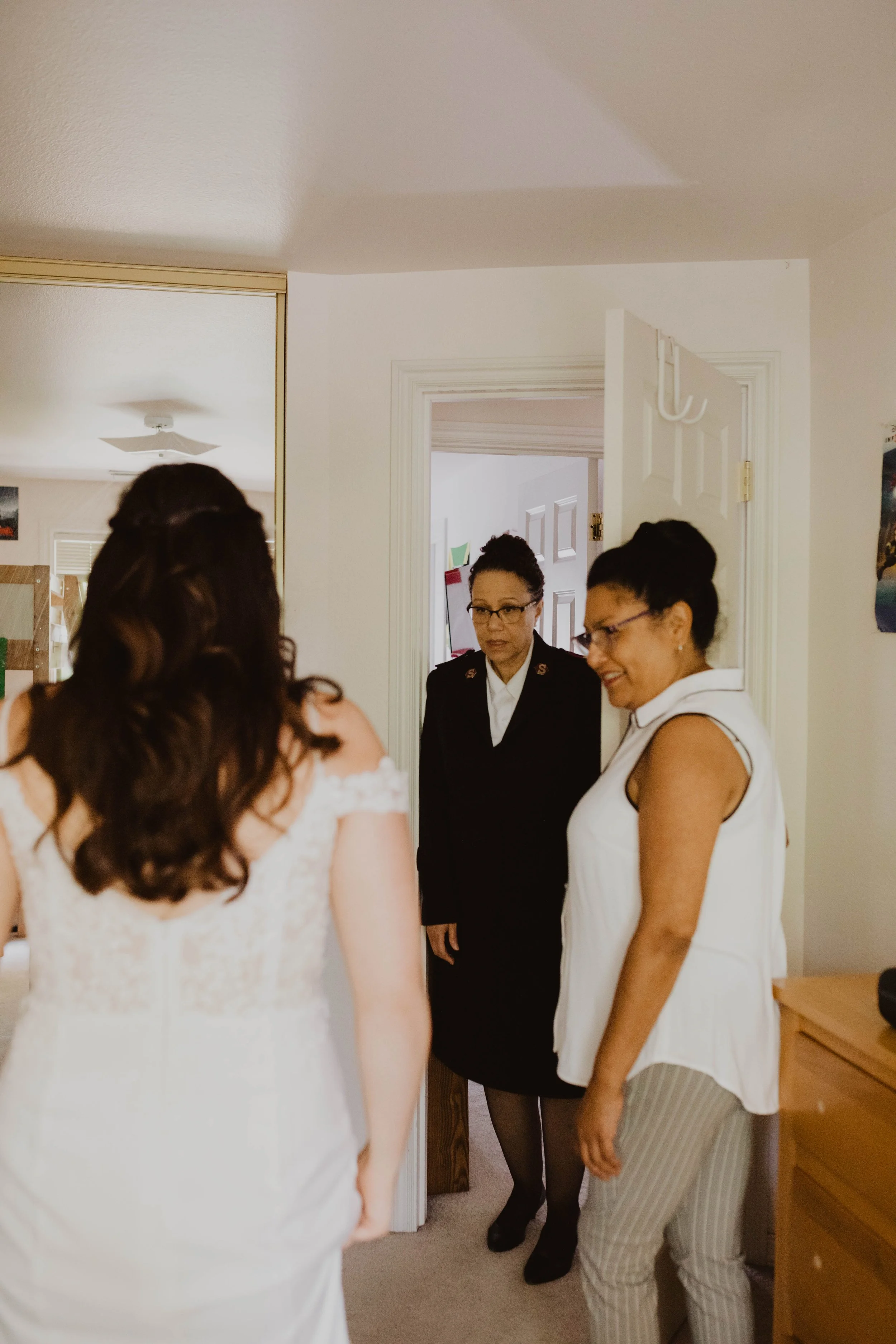 A woman in a wedding dress stand facing two women in casual and business attire inside a home. Seattle, WA wedding photography.