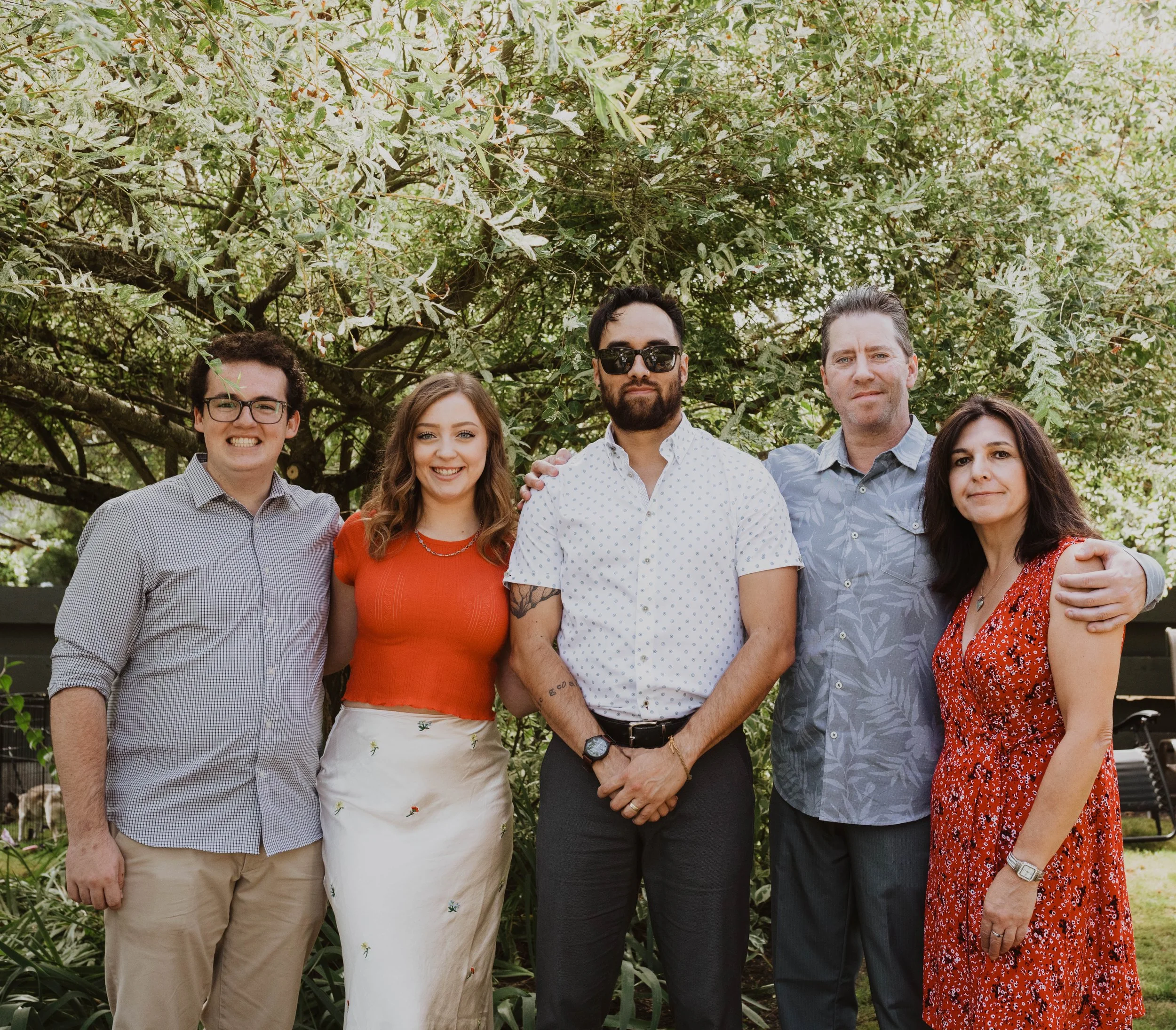 A group of five people standing outdoors under a large green tree, posing for a photo and smiling. Seattle, WA wedding photography.
