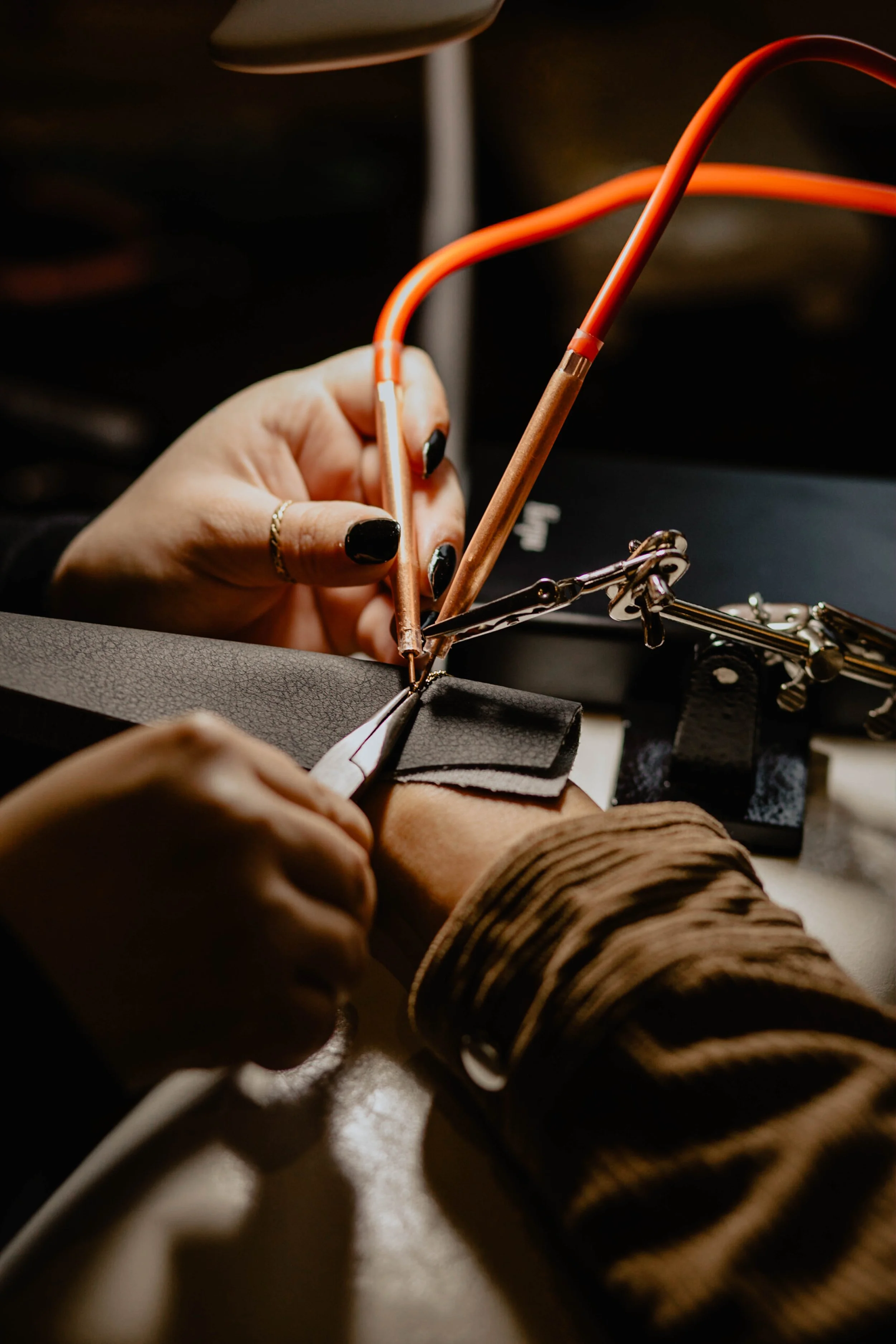 A person using jewelry-making tools, including pliers, to assemble a piece of jewelry with black and metallic components on a workbench. Seattle professional head shot photography