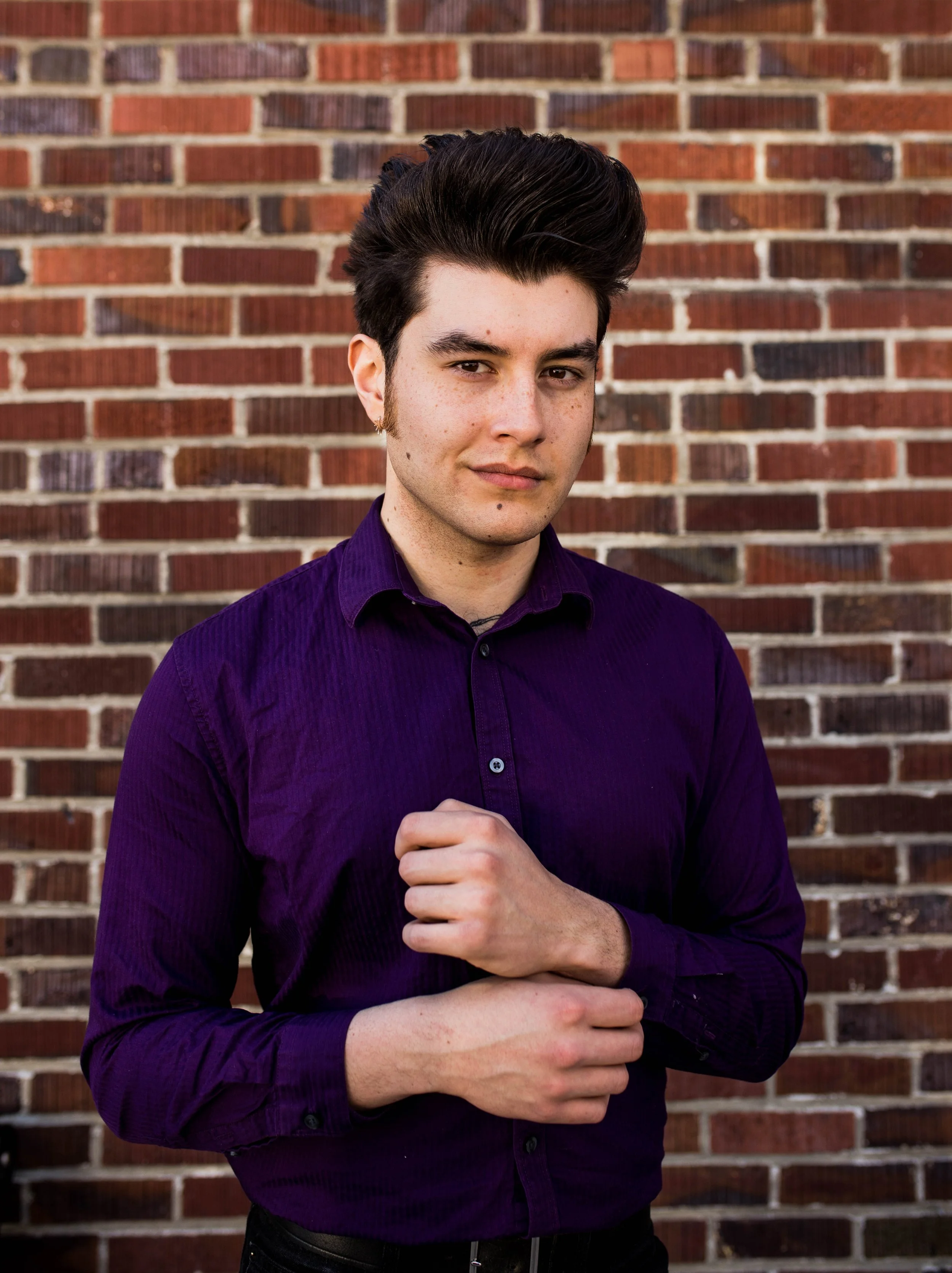 A young man with dark, styled hair wearing a purple button-up shirt standing in front of a brick wall. Seattle professional head shot photography