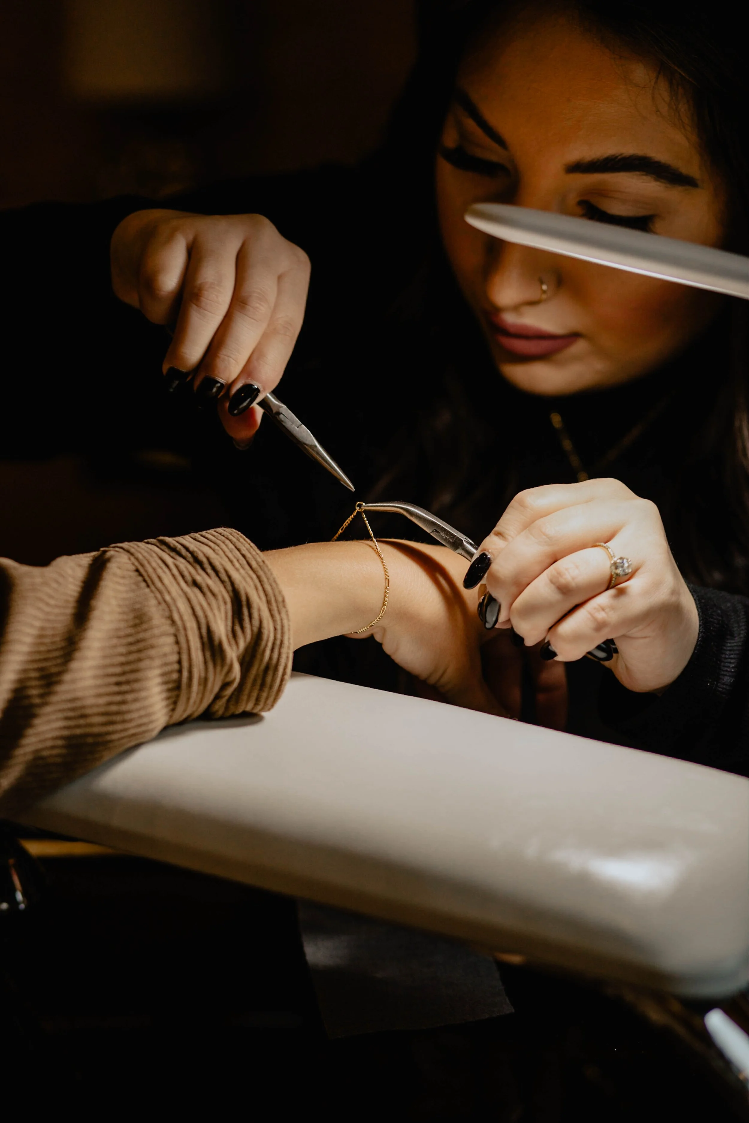 A jewelry artist is crafting a bracelet on a customer's wrist, using jewelry-making tools in a dimly lit studio. Seattle professional head shot photography