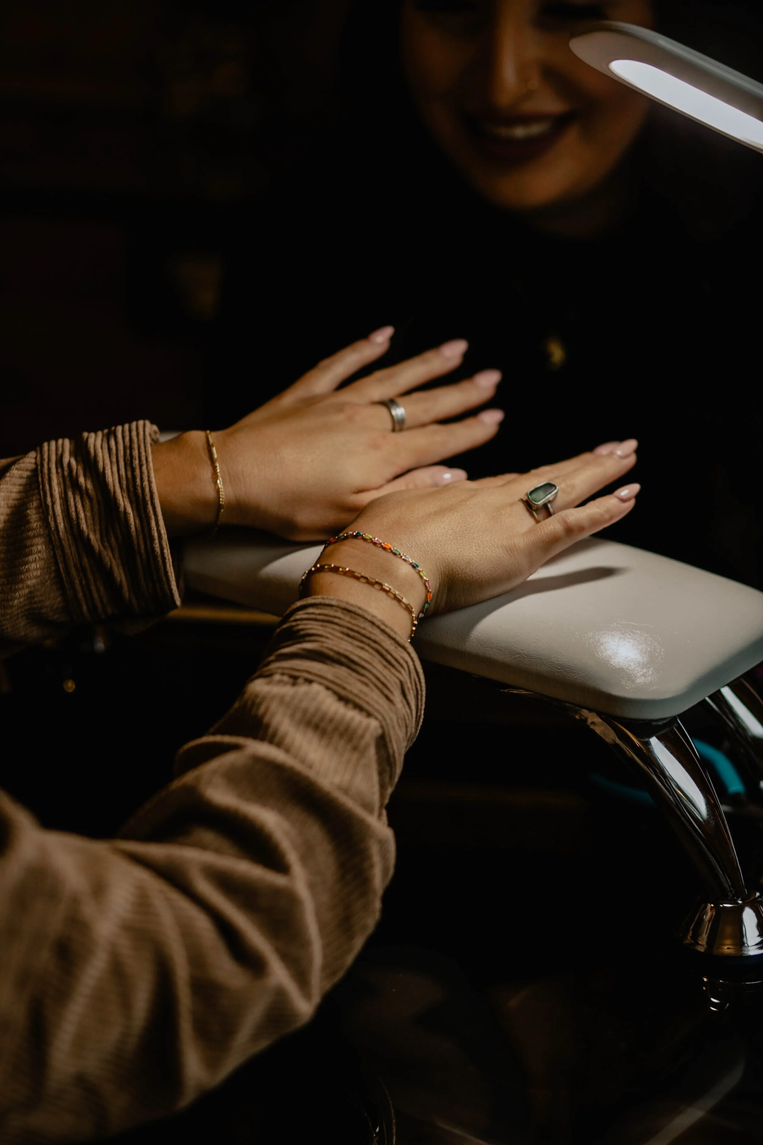 Hands with rings and bracelets resting on a padded surface, with a smiling woman in the background illuminated by a ring light. Seattle professional head shot photography
