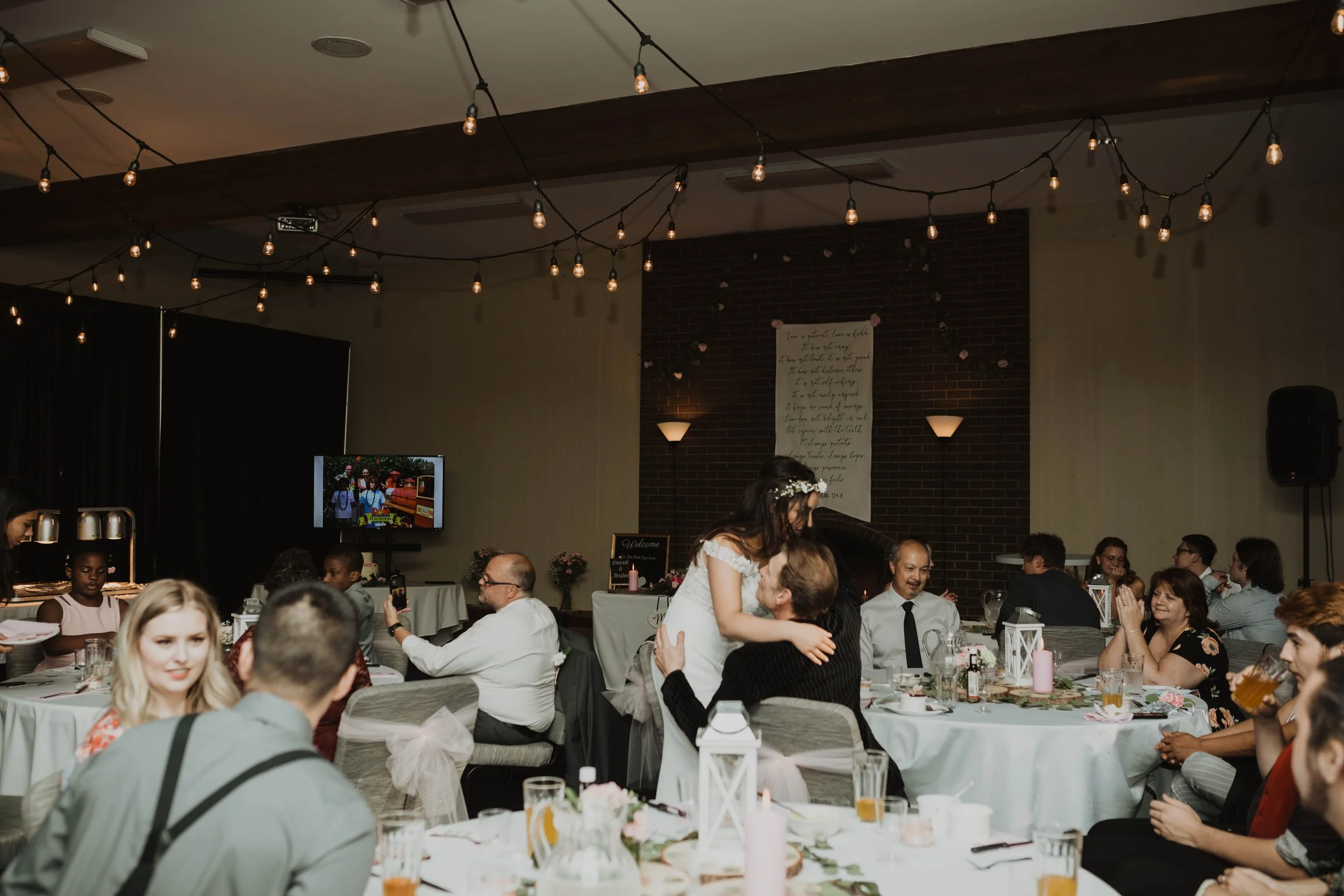Wedding reception with guests seated at tables, a bride and groom dancing, string lights overhead, and a fireplace with a quote on the wall Seattle, WA wedding photography.