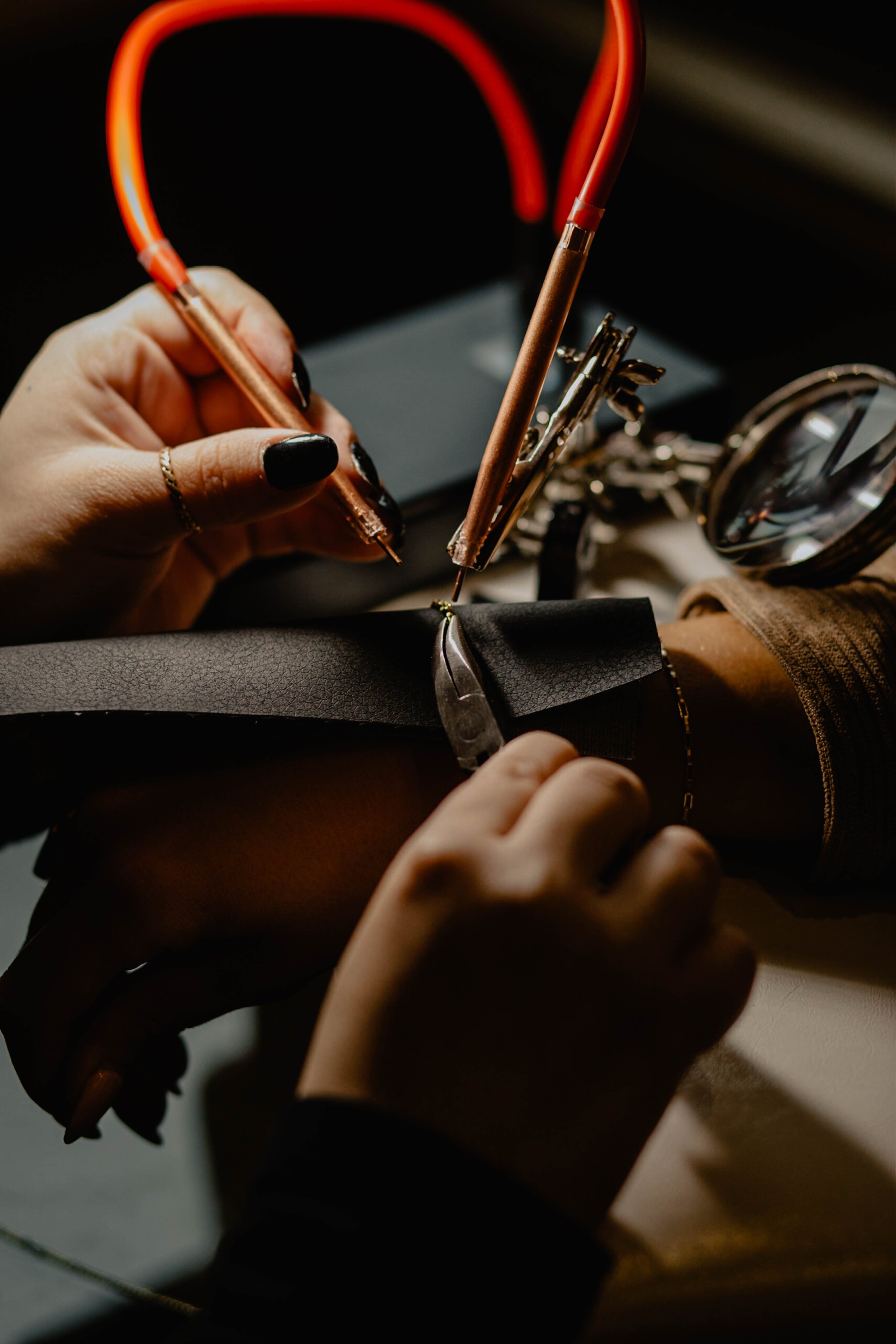A person sewing black leather material with a copper-colored sewing machine in a dimly lit environment. Seattle professional head shot photography
