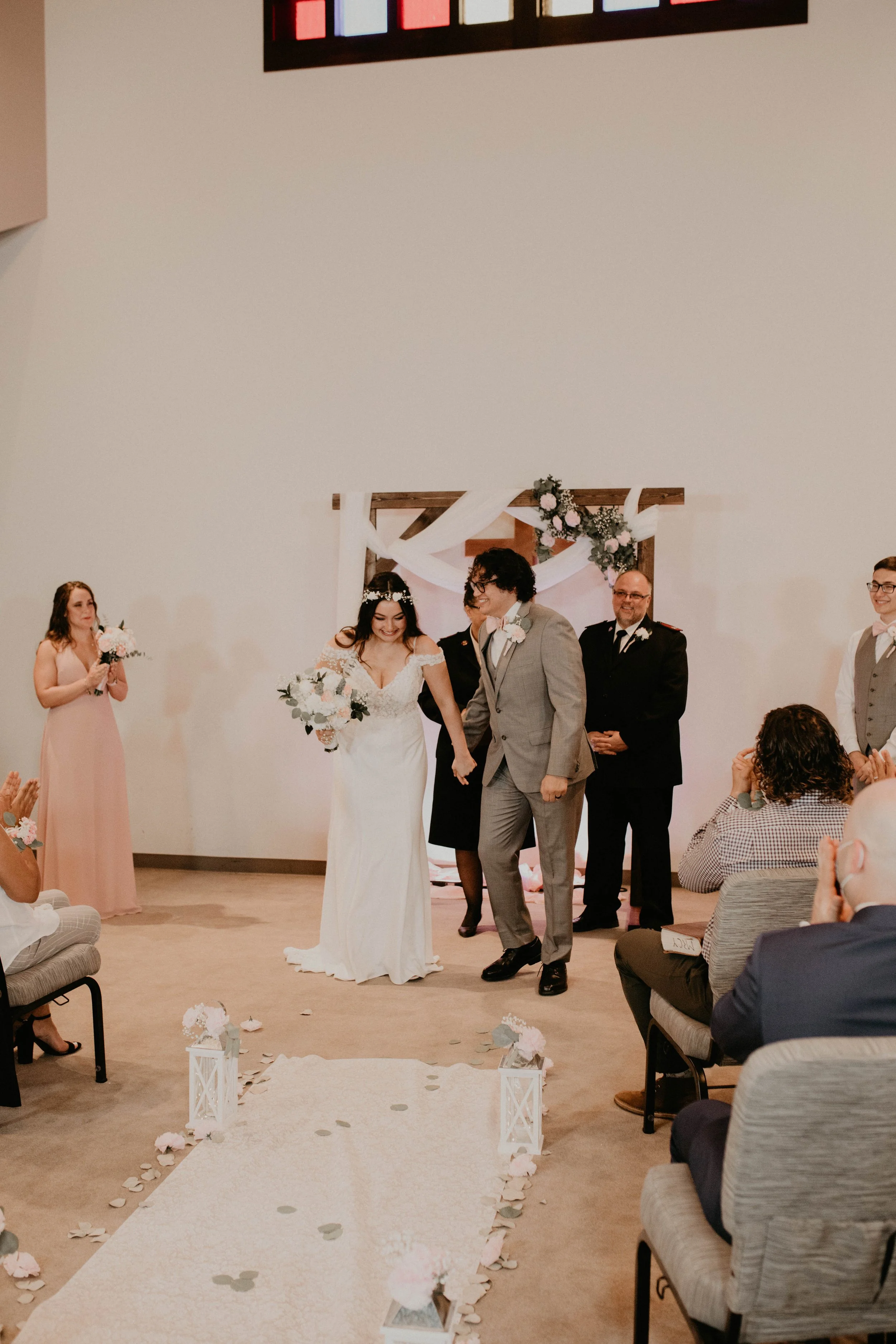 A wedding ceremony with a bride and groom walking down the aisle, surrounded by seated guests and wedding party members, in a decorated indoor venue. Seattle, WA wedding photography.