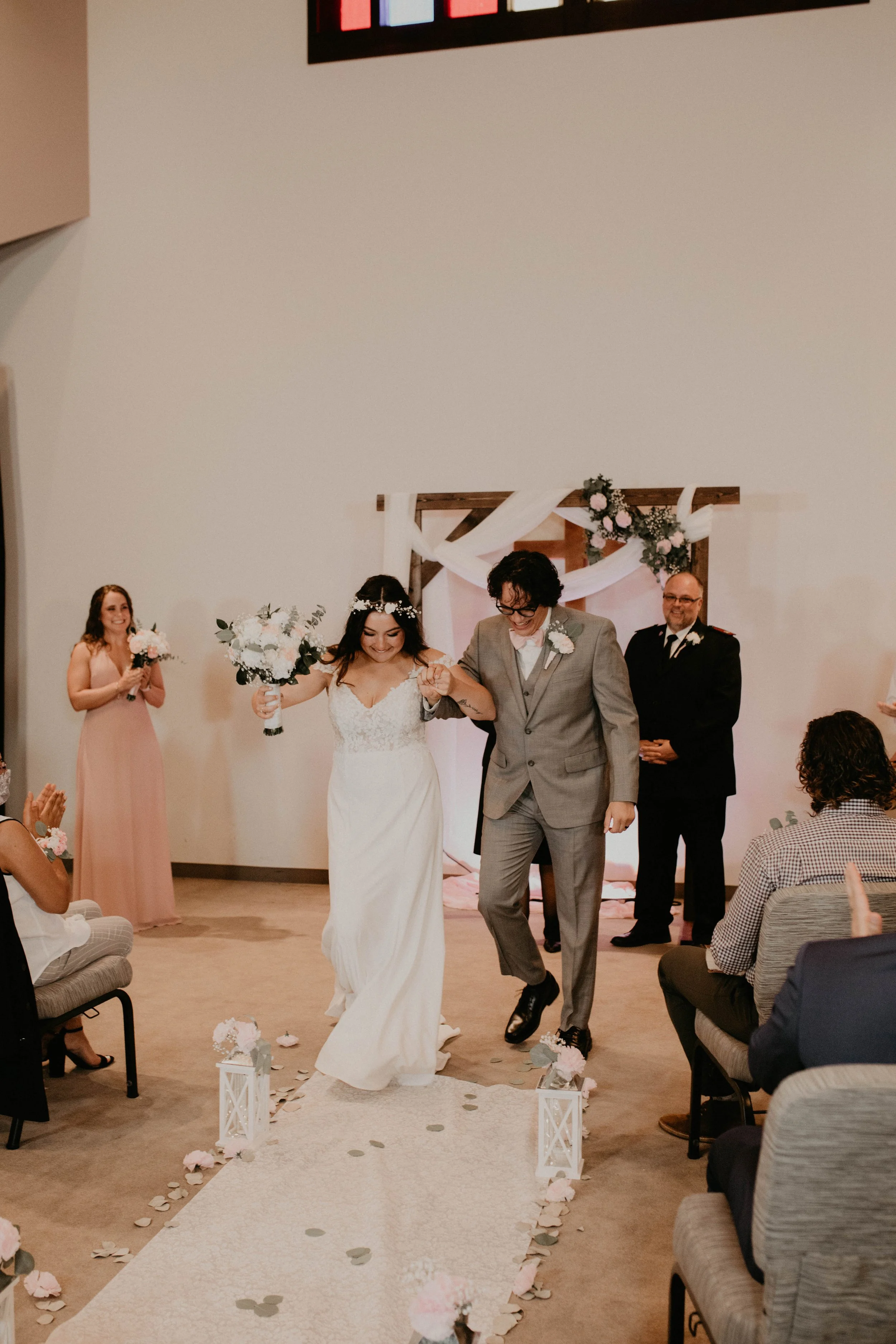 Bride and groom walking down the aisle at a wedding ceremony, with guests clapping and flowers decorating the aisle. Seattle, WA wedding photography.