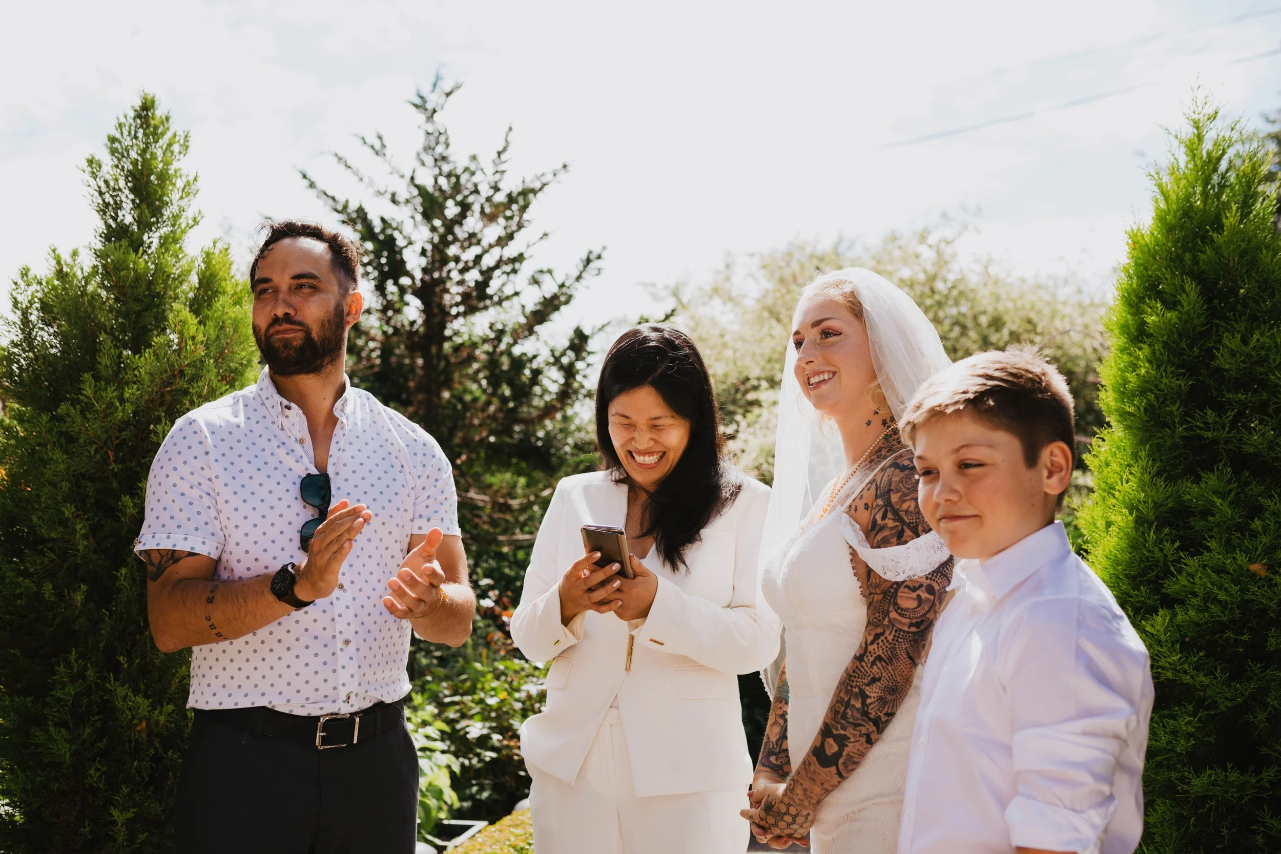 Group of five people outdoors, including a man and woman dressed for a wedding, with others smiling and laughing. Seattle, WA wedding photography.