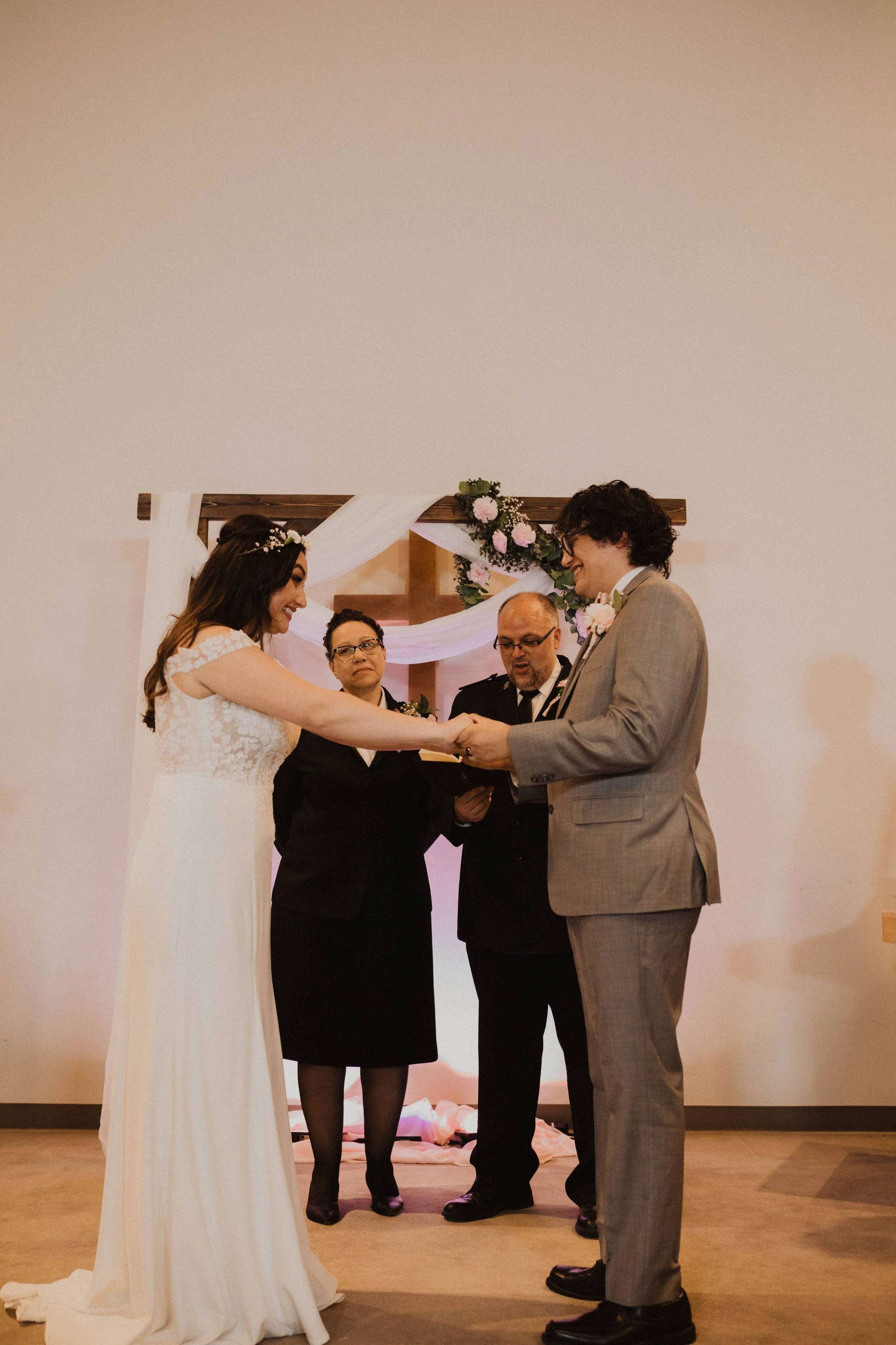 A couple gets married, holding hands during the wedding ceremony, with two officiants standing behind them and a decorated wedding arch in the background. Seattle, WA wedding photography.